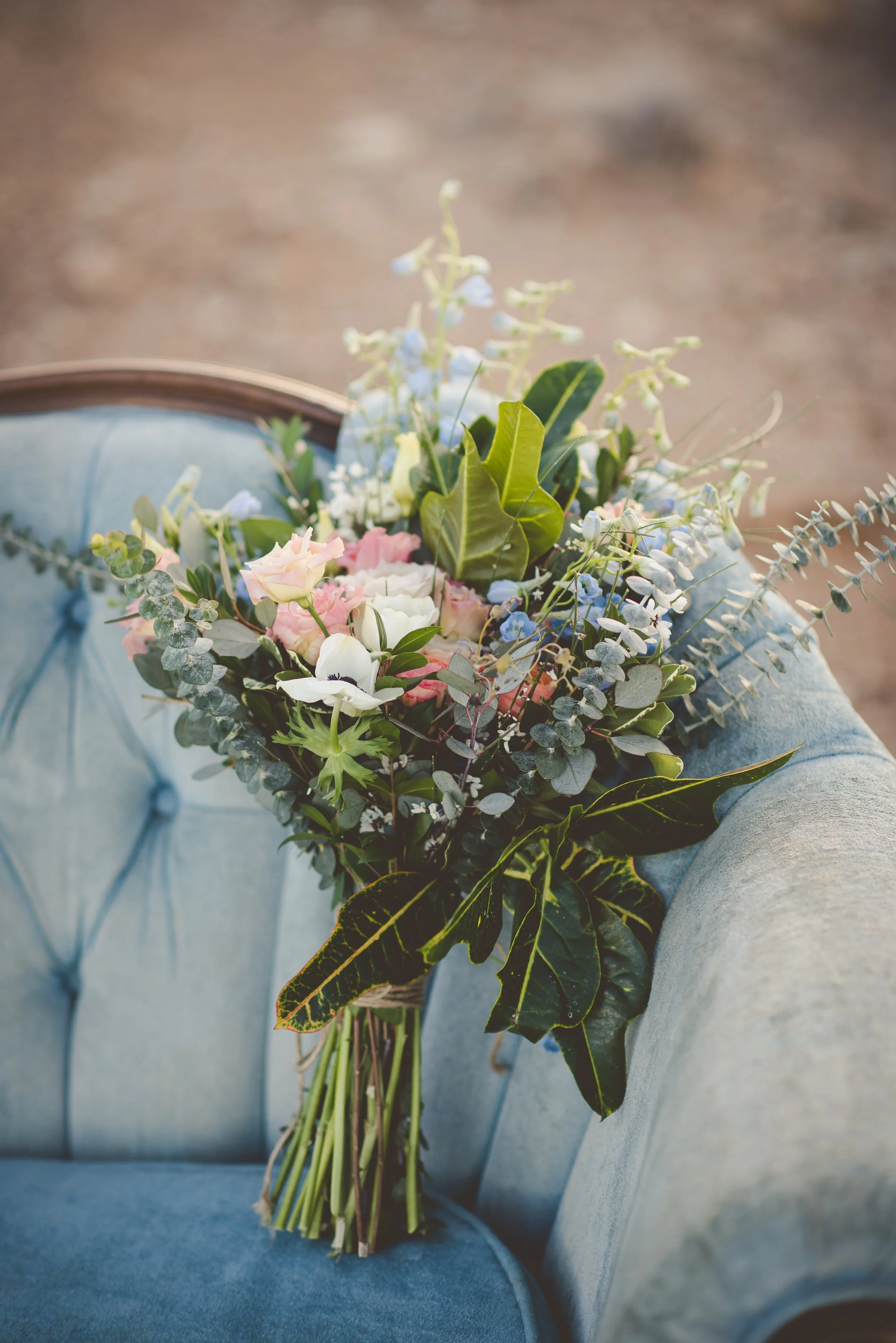 Bouquet of assorted flowers and green foliage resting on a light blue upholstered chair.