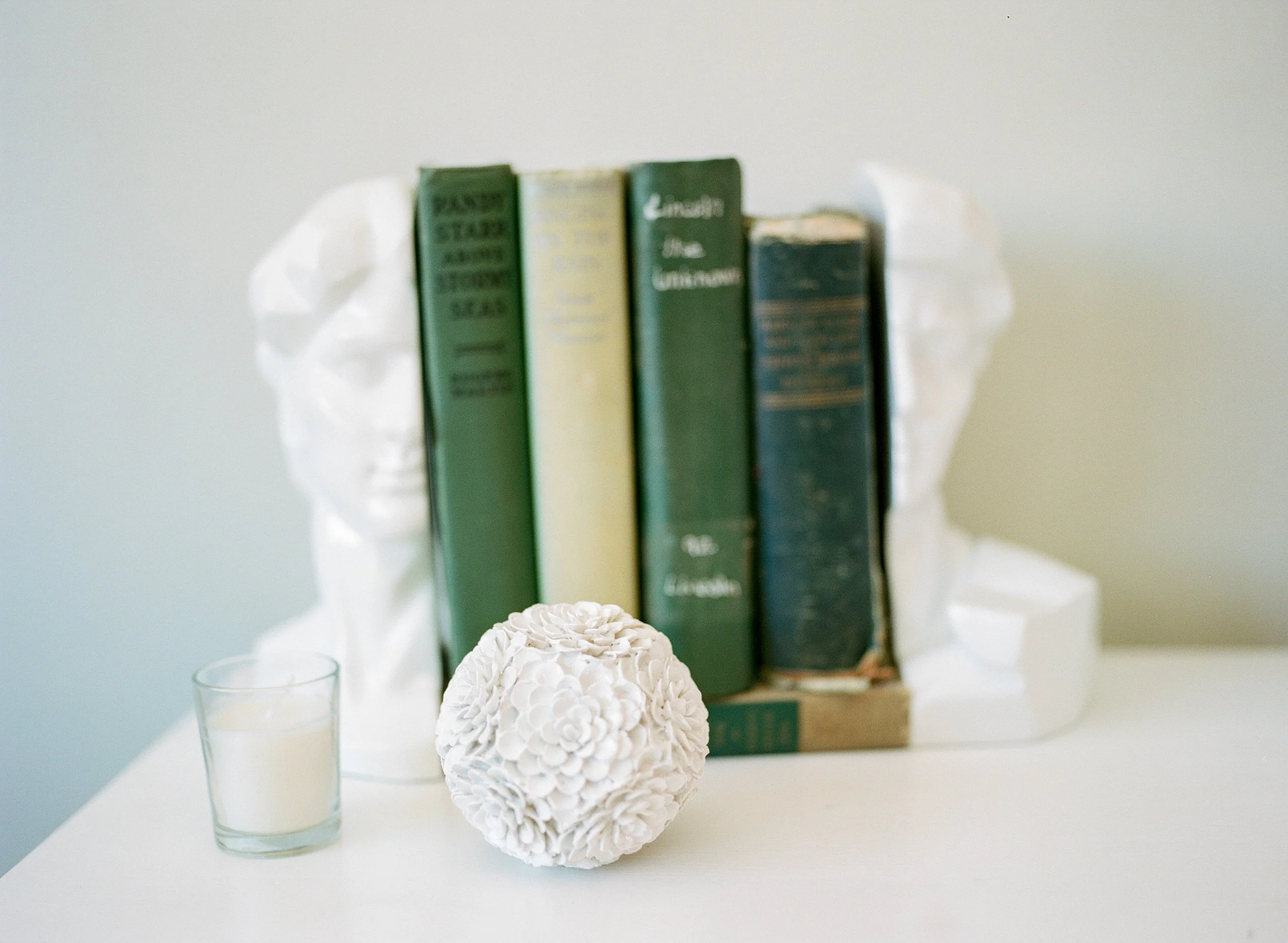 A white decorative sculpture, a glass of milk, and a stack of old books on a white surface and background.