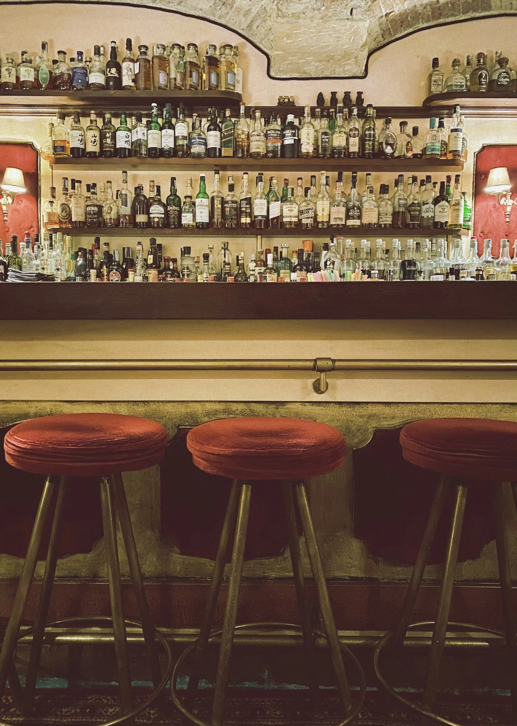 Bar with shelves of liquor bottles and four red bar stools in front