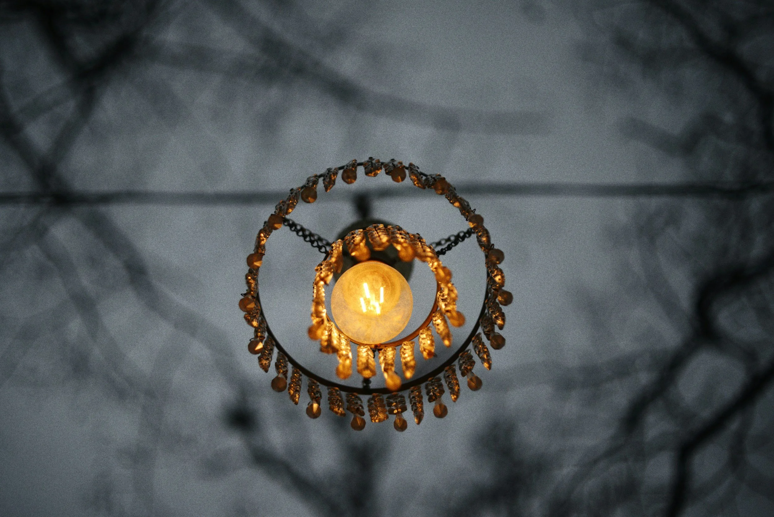 A chandelier hanging from a ceiling with a decorative chain and beads, illuminated and creating a warm glow in the surrounding space.