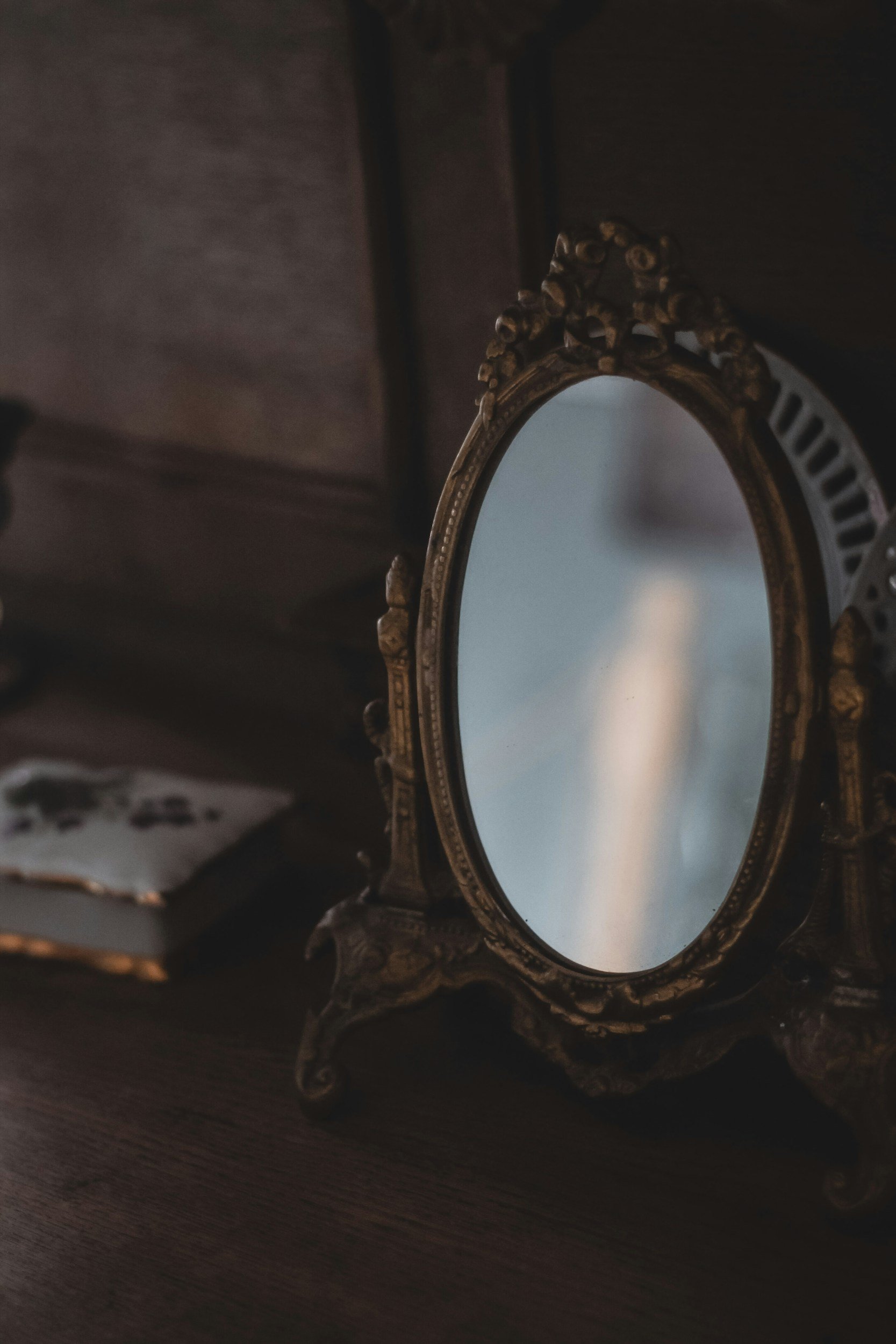 An ornate, vintage-style mirror with a decorative frame resting on a dark surface.