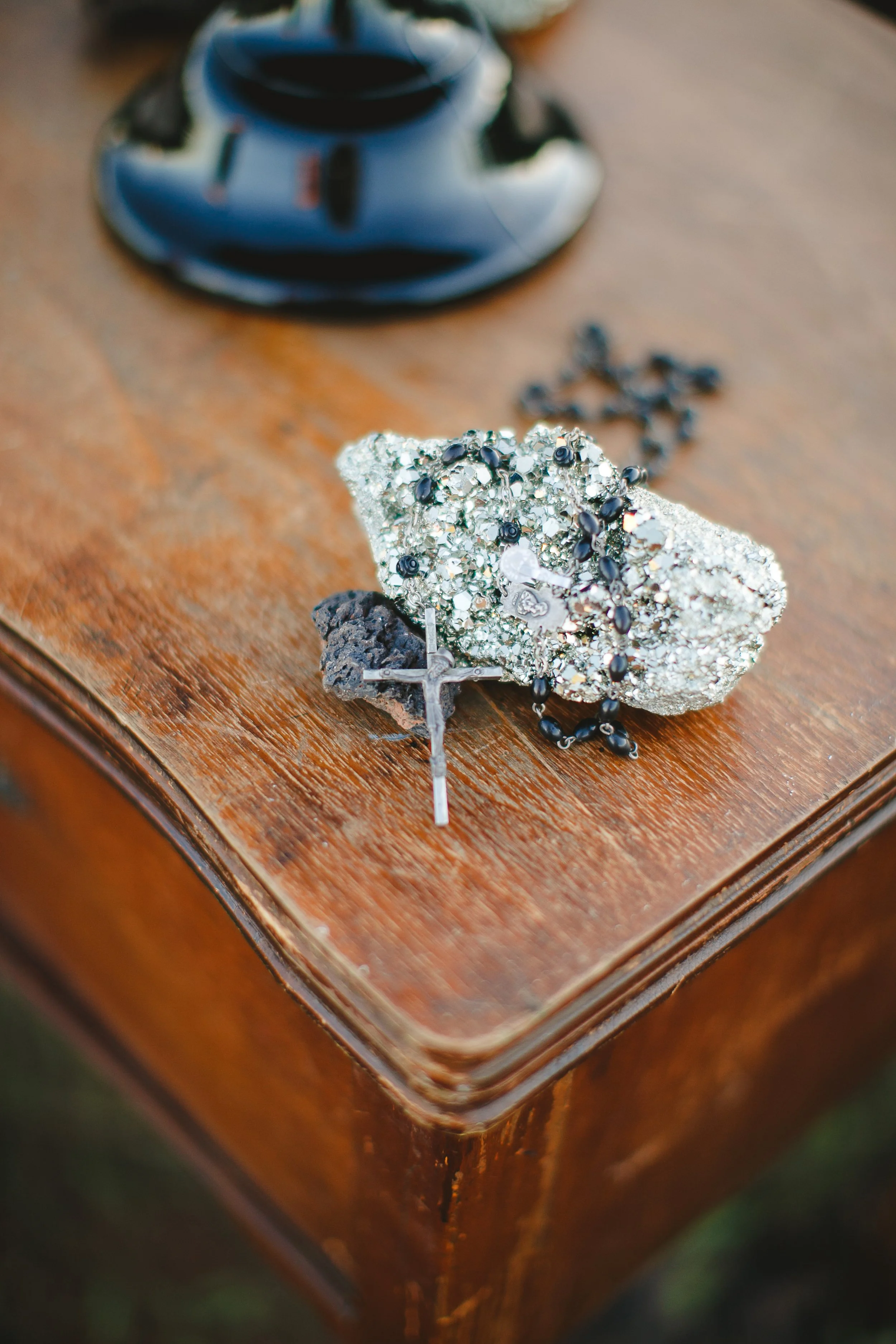 A decorative butterfly brooch with black and silver details on a wooden surface, with a blurred black camera lens in the background.