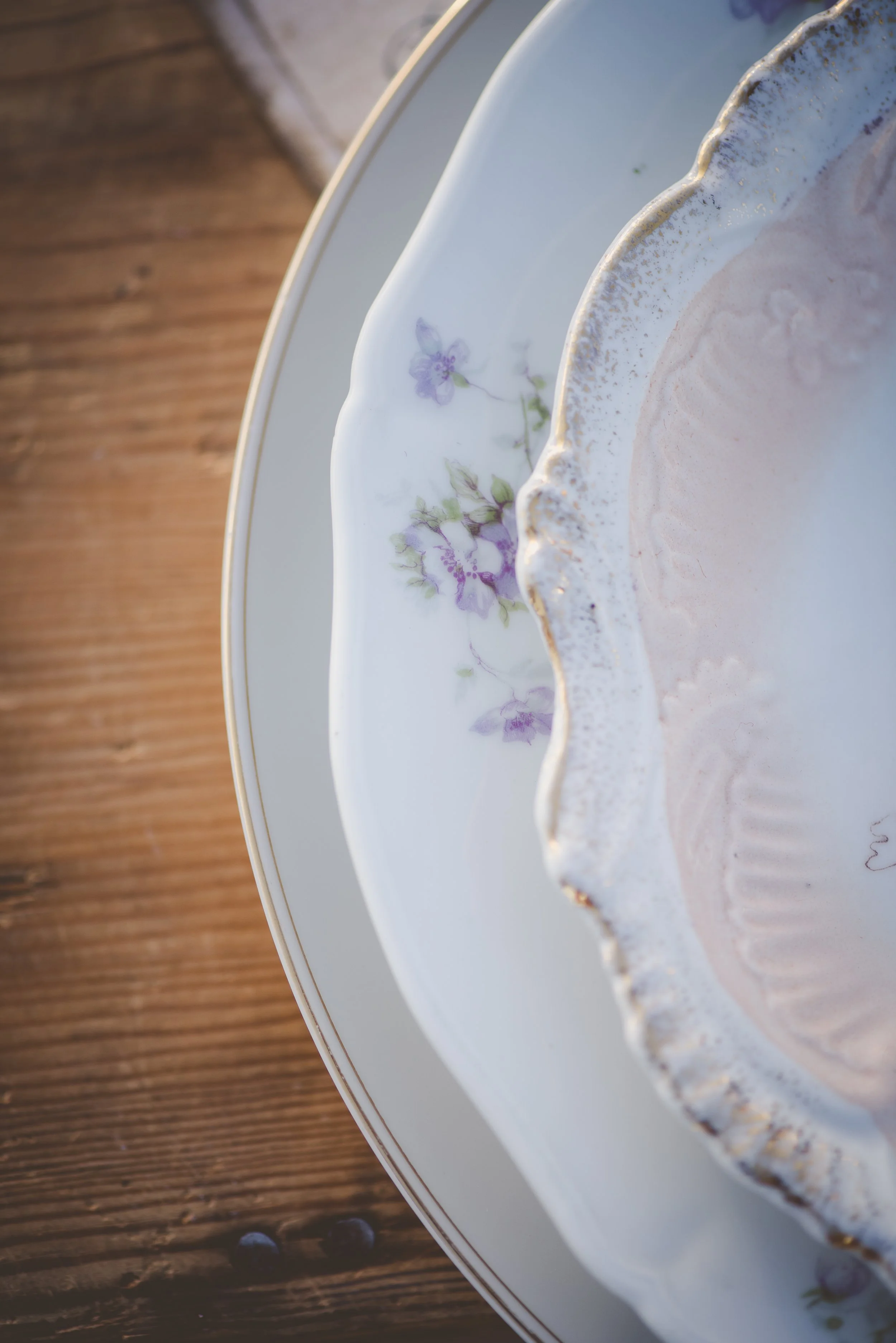 Close-up of a decorative porcelain plate with a purple floral pattern and gold rim, on a wooden surface.