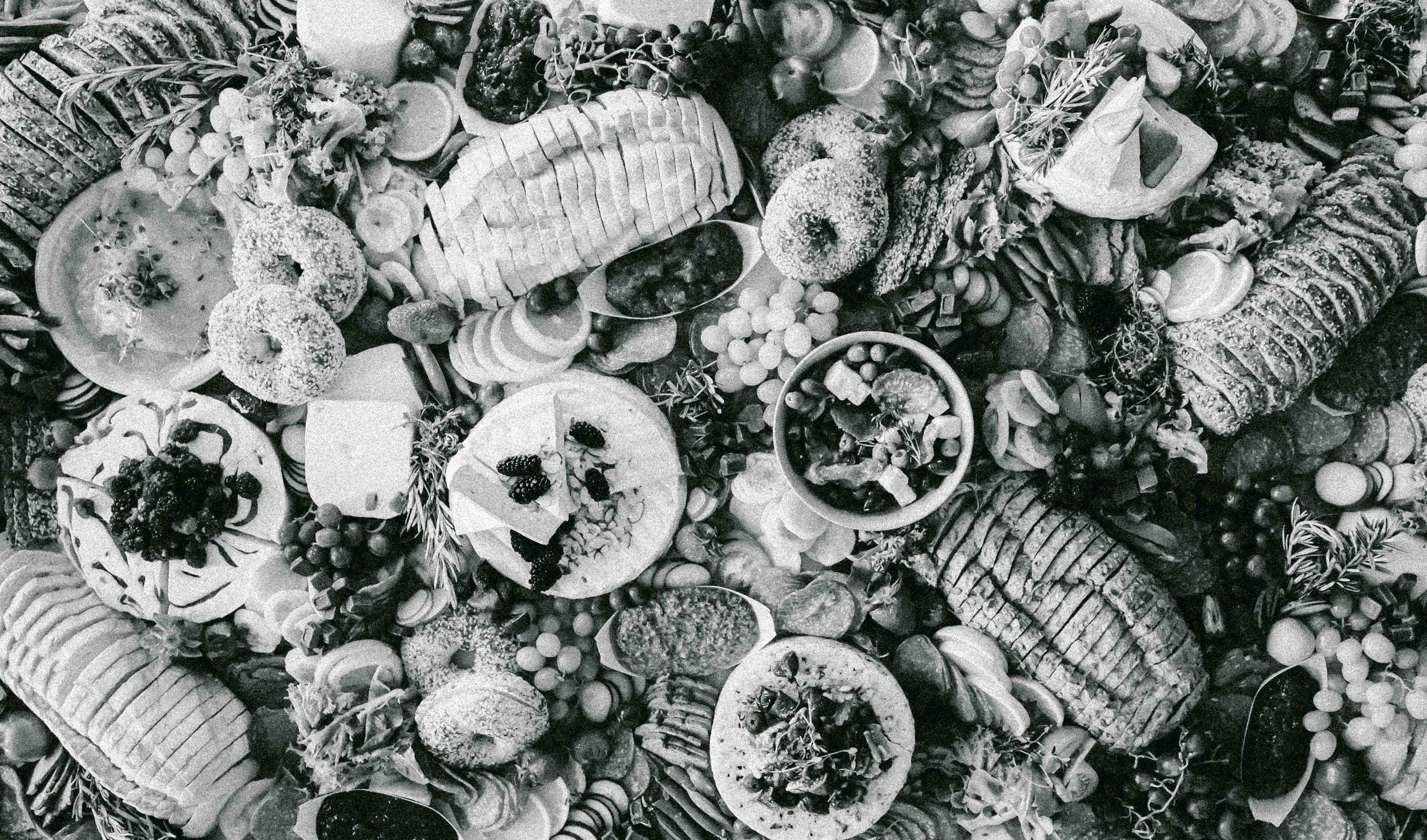 A large platter filled with various appetizers, including sliced meats, cheeses, crackers, grapes, olives, and garnishes.