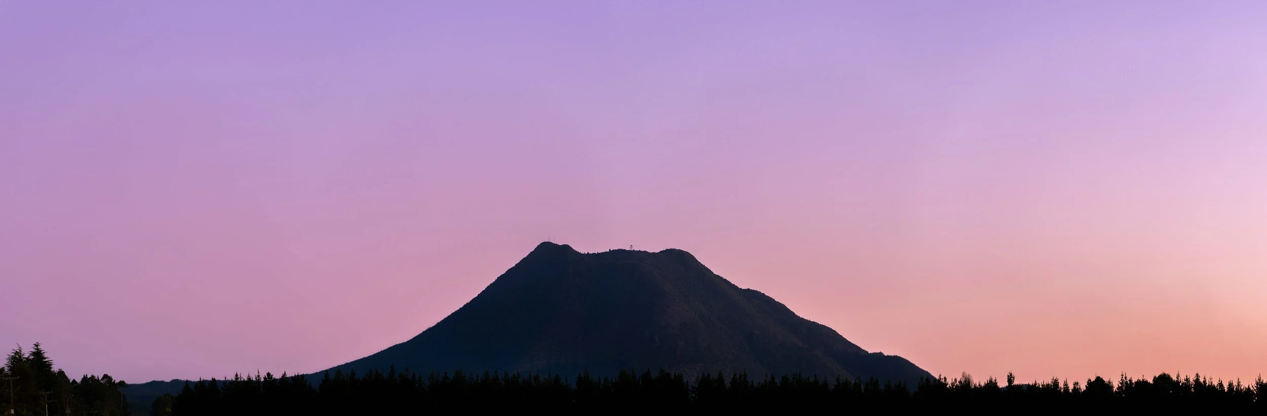 A silhouette of a mountain at sunset with a clear, colorful sky in shades of purple and pink.