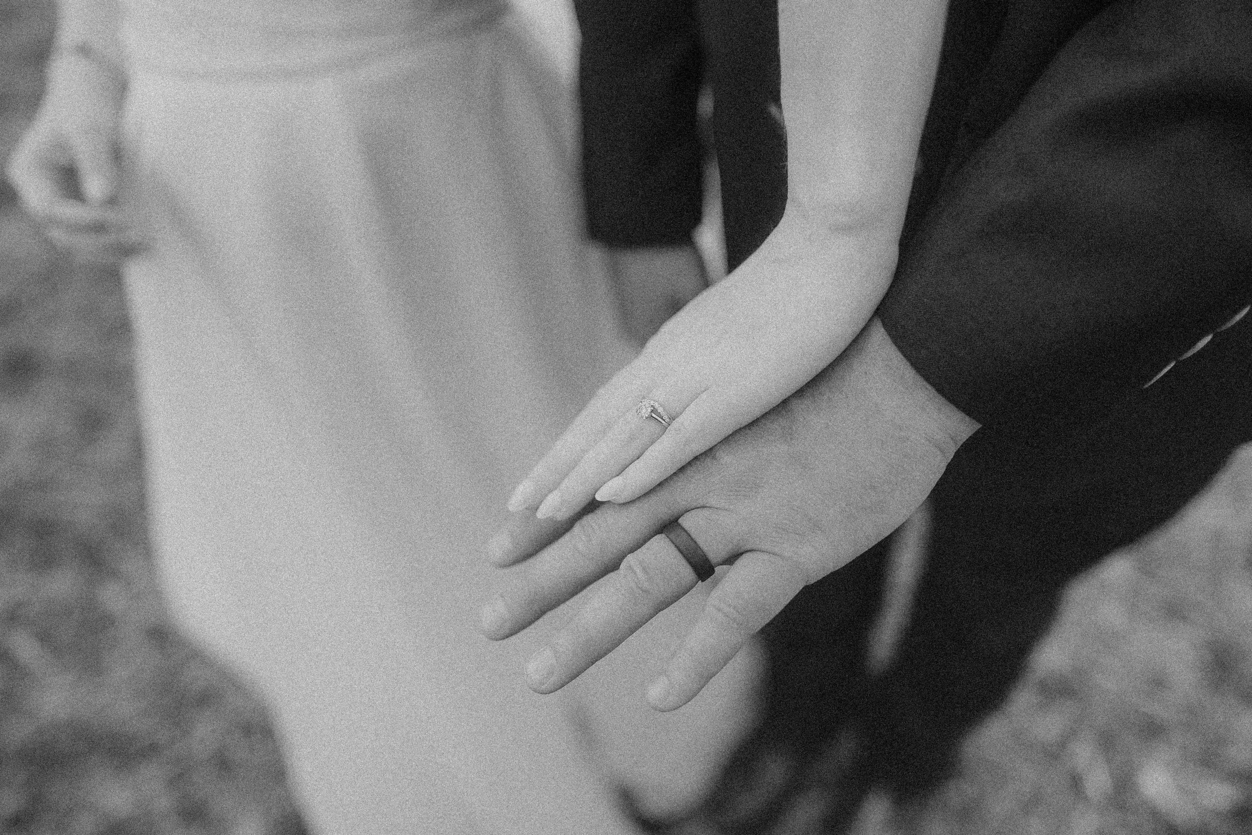 Close-up of a couple holding hands, with the woman wearing a ring on her finger.