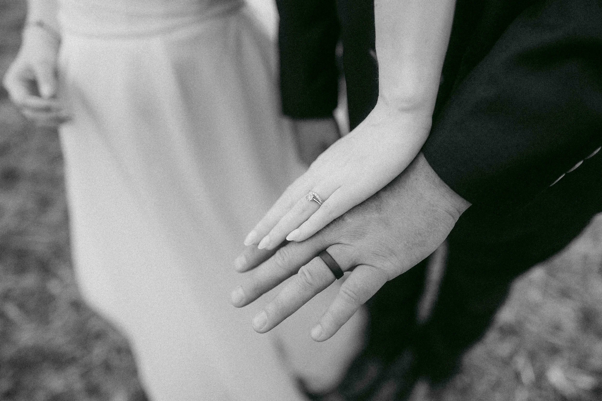 Close-up of two people holding hands, one person wearing a ring, in an intimate gesture.
