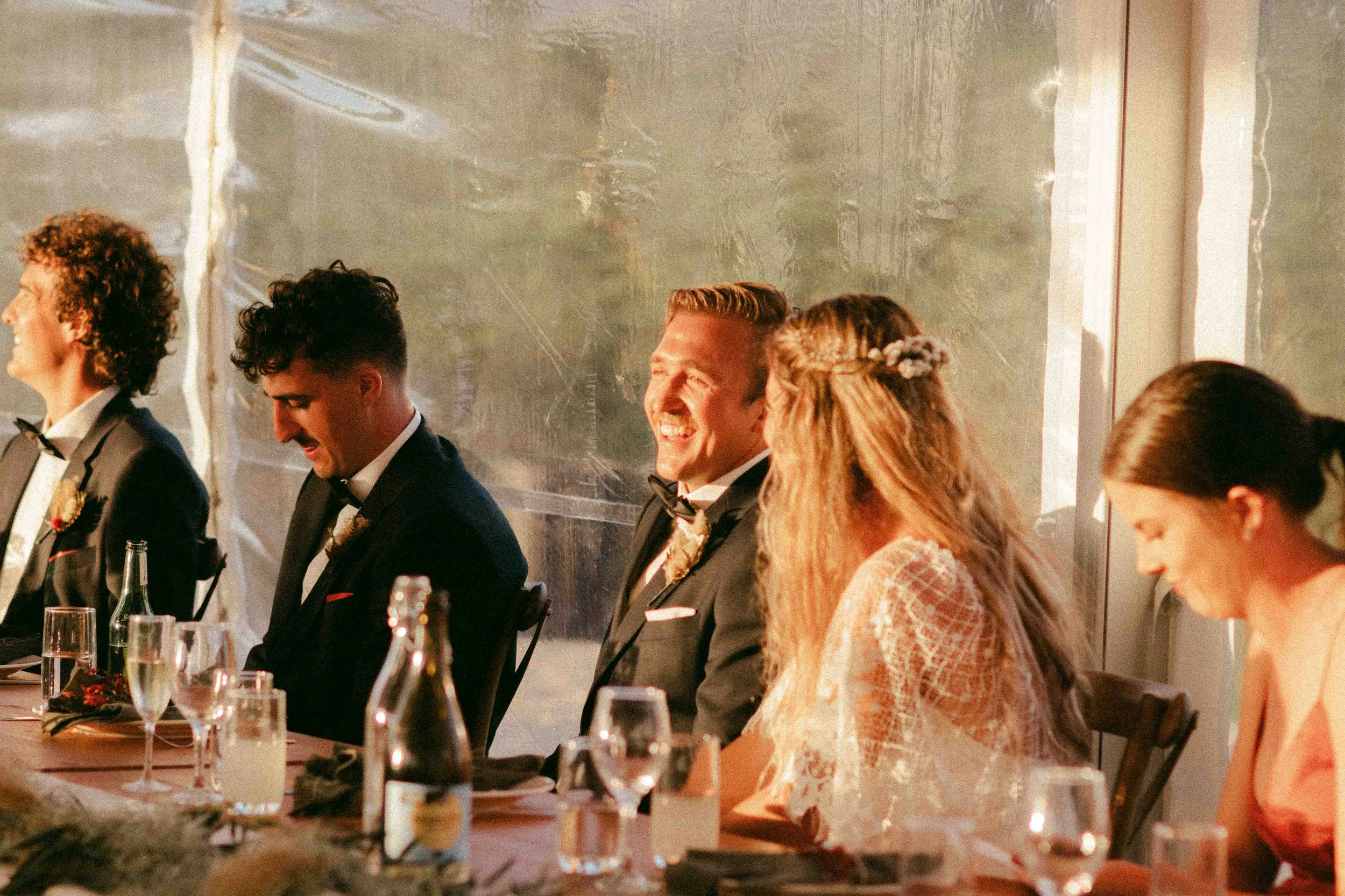 People dressed in formal attire seated at a banquet table, smiling and laughing during a celebration or wedding reception.