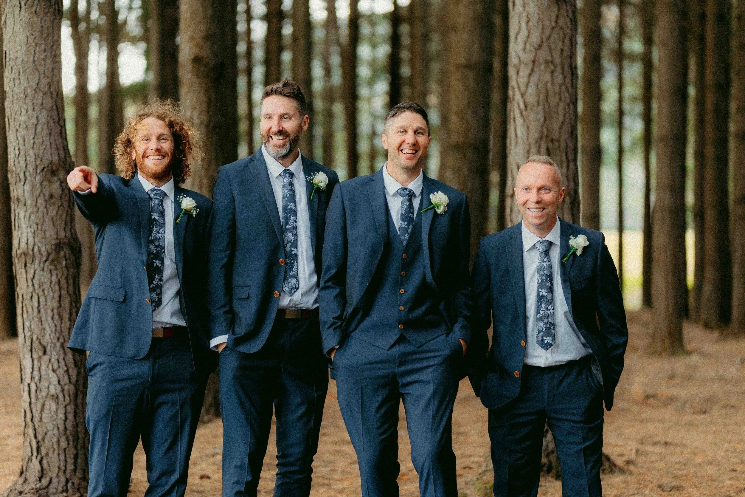 Five men dressed in suits walking in a wooded area, smiling and enjoying each other's company.