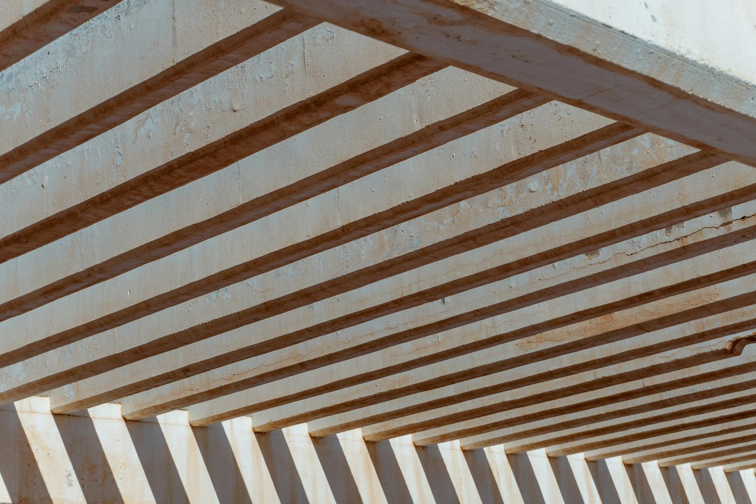 Close-up of wooden beams with sunlight casting shadows on a concrete wall.
