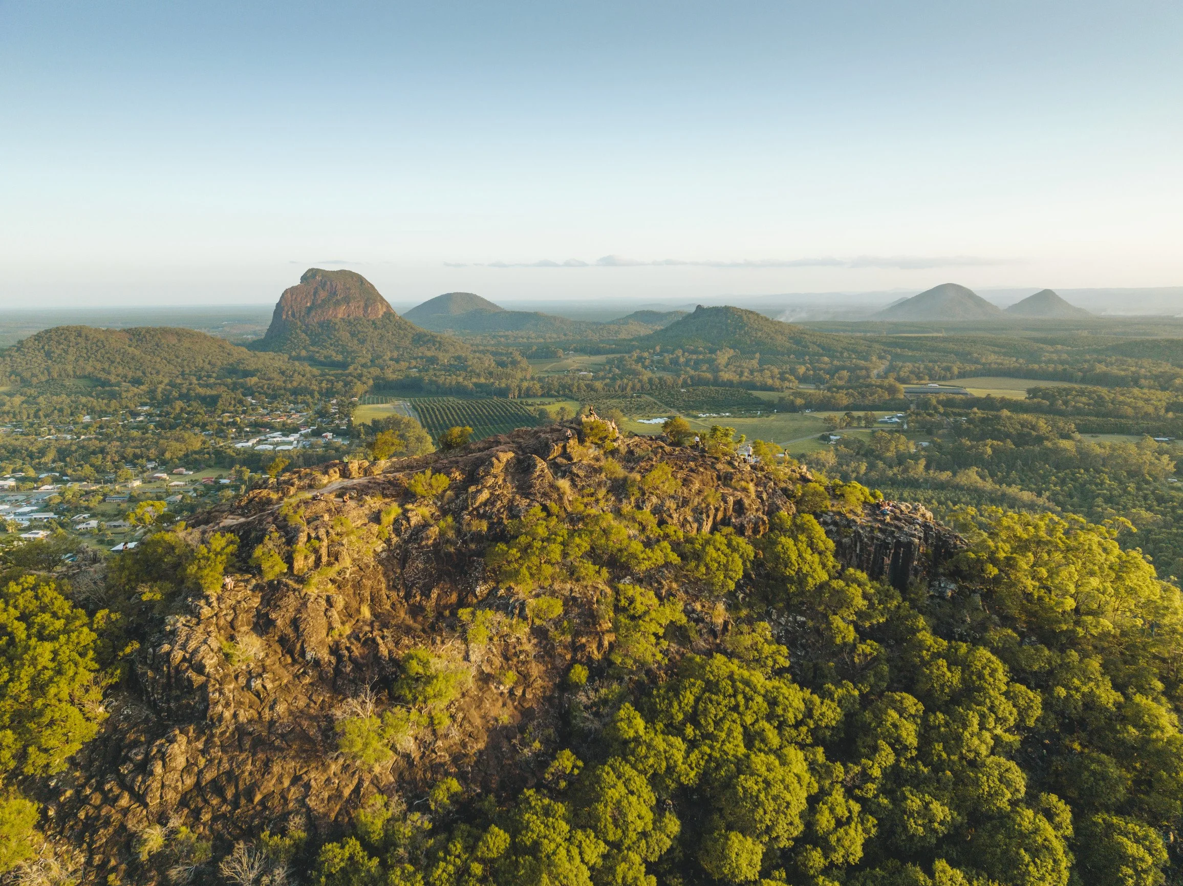 A vast landscape with lush green trees, rocky hills, and distant mountains under a clear blue sky.
