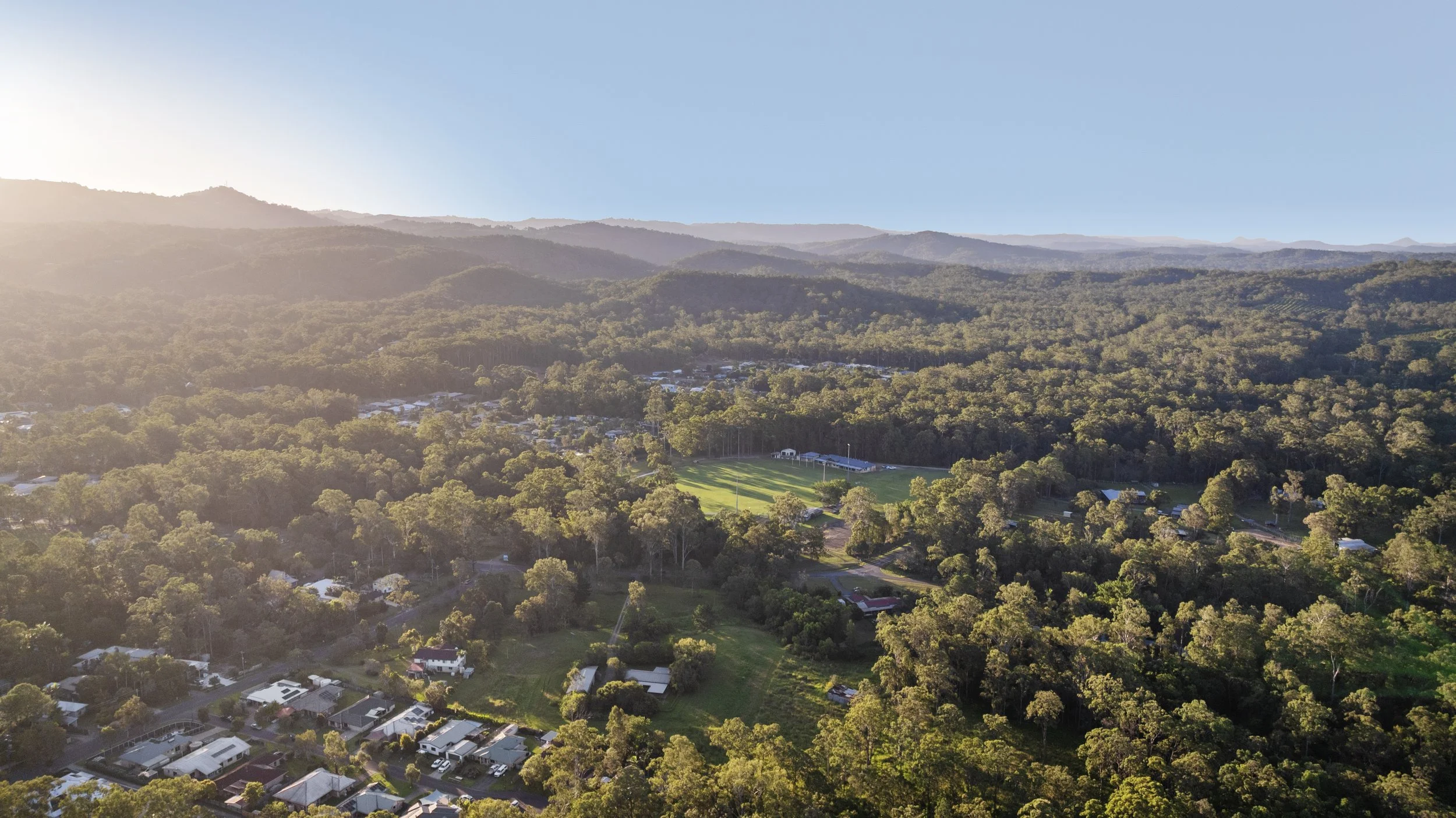 Aerial view of a town surrounded by lush green forest with mountains in the background, during sunset.