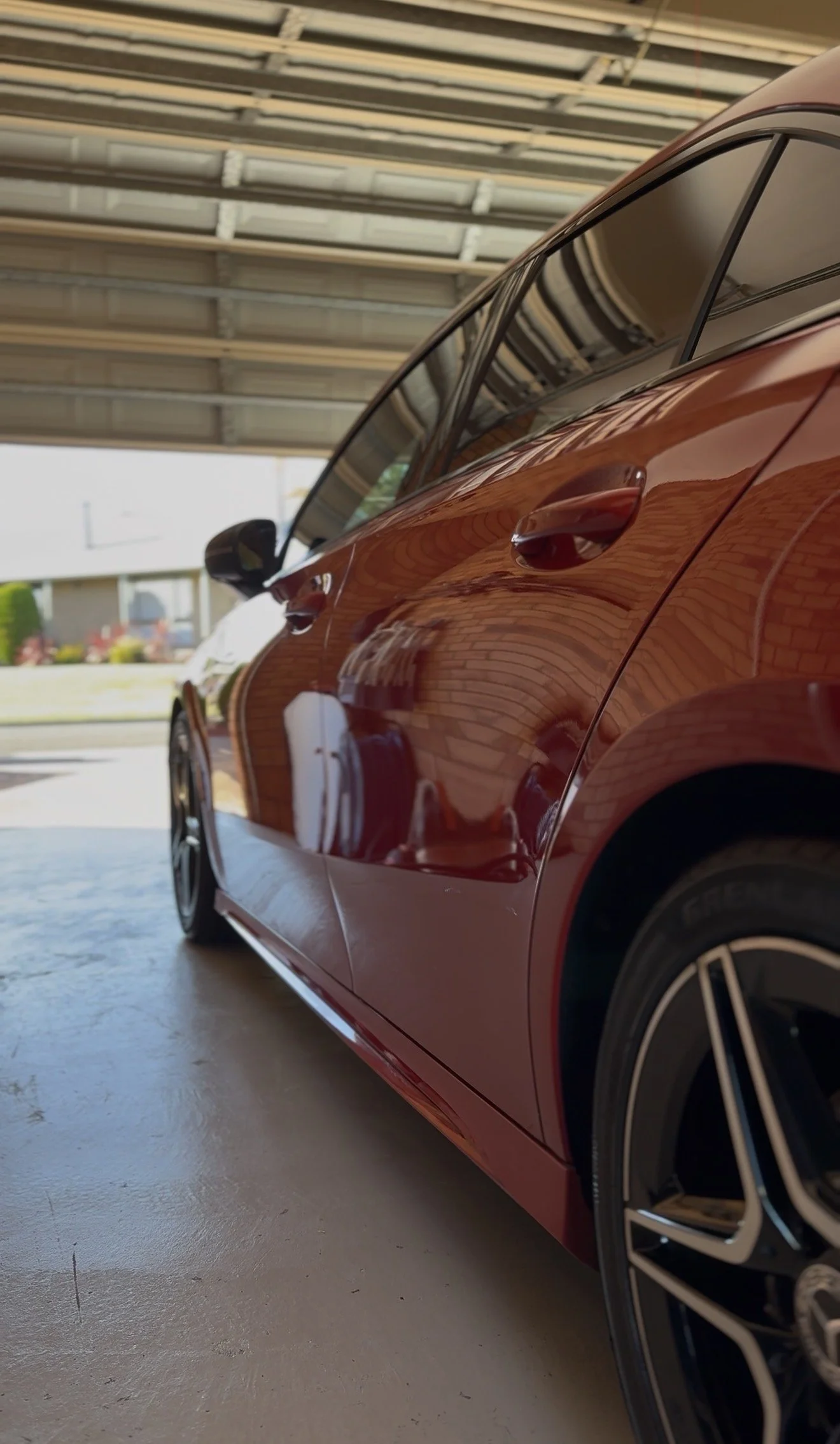 Close-up of a shiny red car parked inside a garage with a concrete floor and garage ceiling visible.