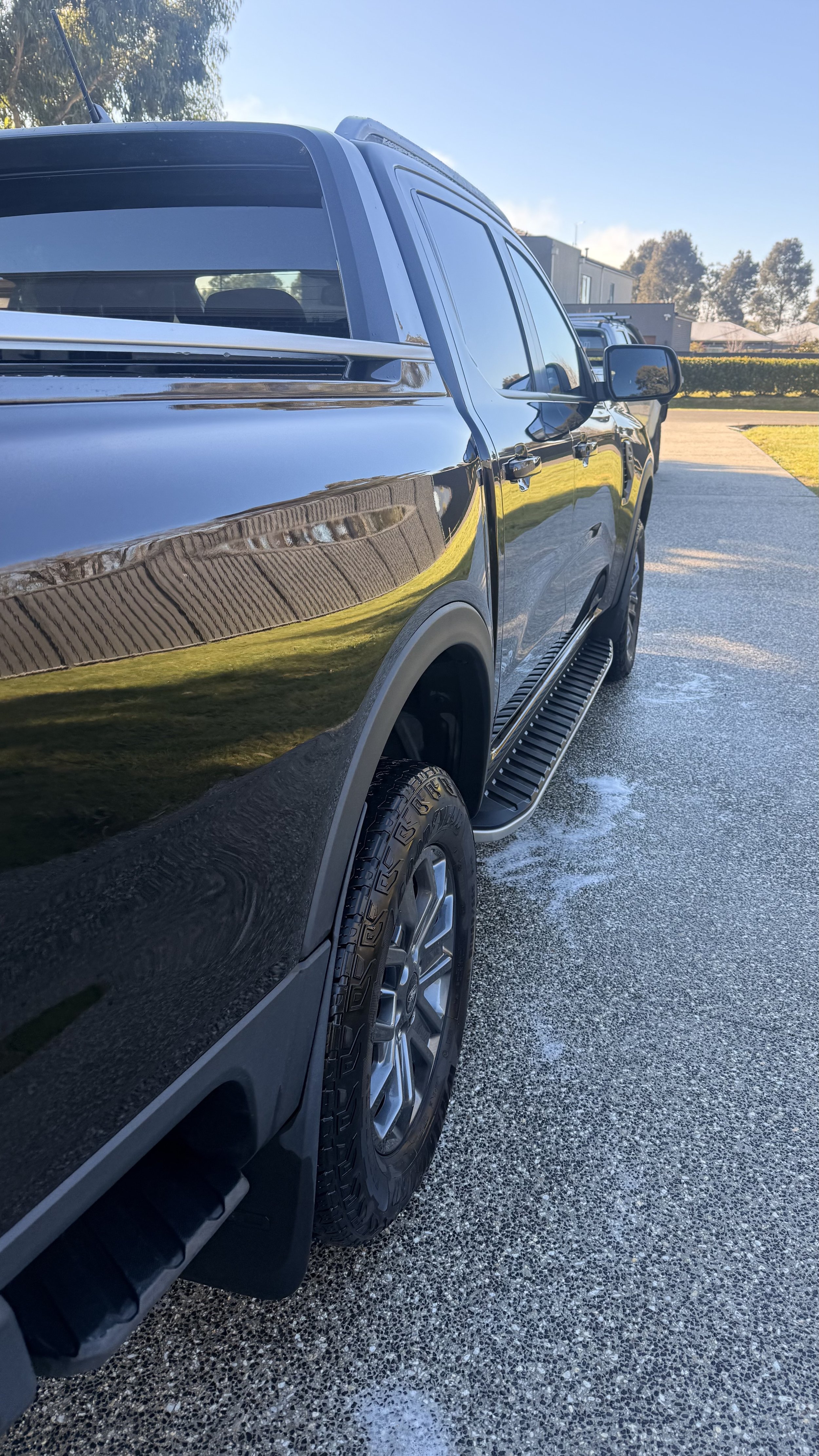 A black pickup truck parked on a driveway on a clear day, with trees and houses in the background.