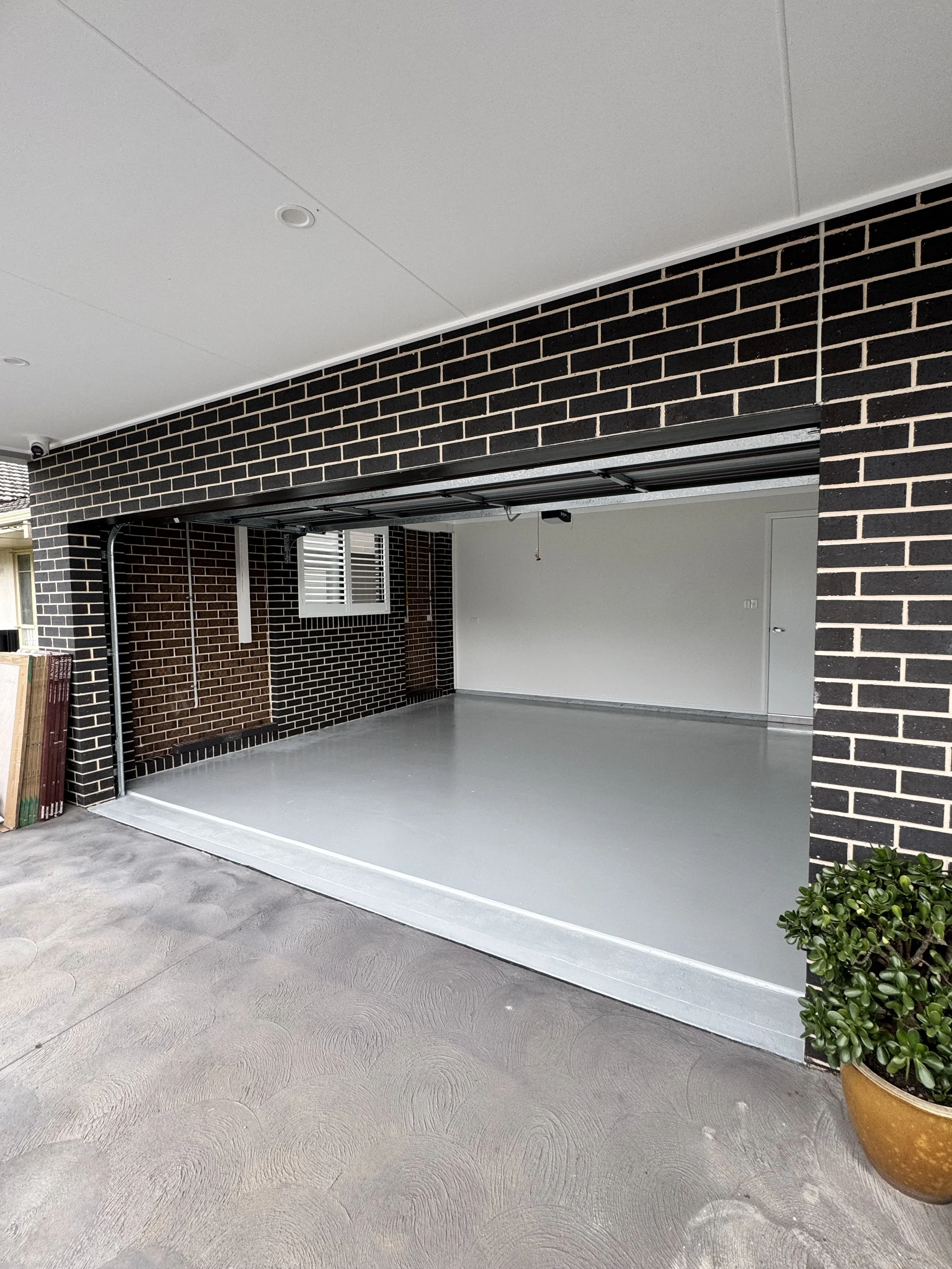 Empty garage with black brick walls, white ceiling, white door, and a potted green plant near the right corner.