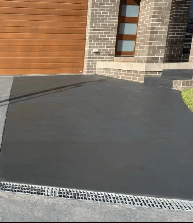 Newly poured black concrete driveway in front of a modern house with a brick and wood garage door.