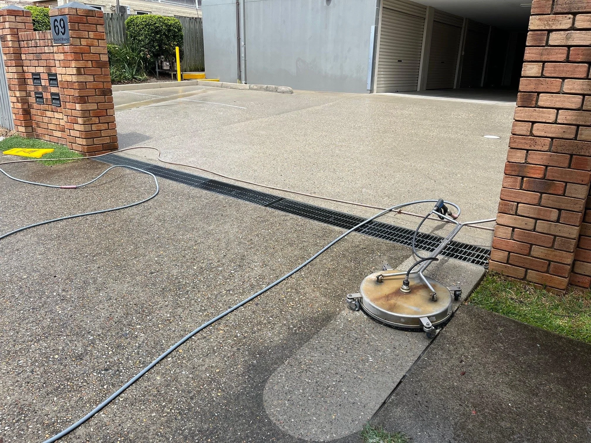 A concrete driveway with a ground-penetrating radar device connected to cables, likely used for underground utility detection, next to a brick wall and a parking area.