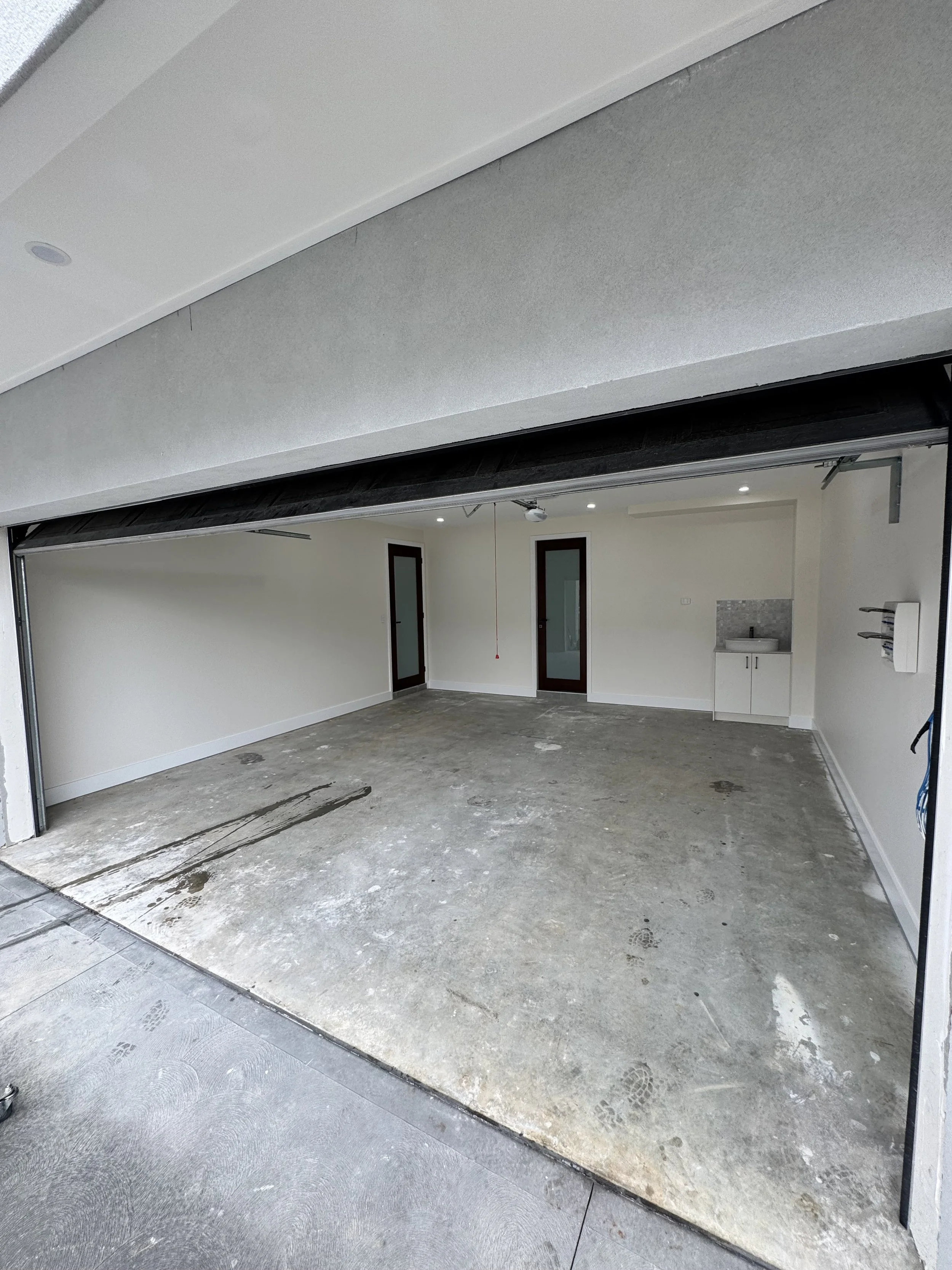 Interior of a garage with an open garage door, showing a concrete floor, white walls, and two partially visible glass-paneled doors.