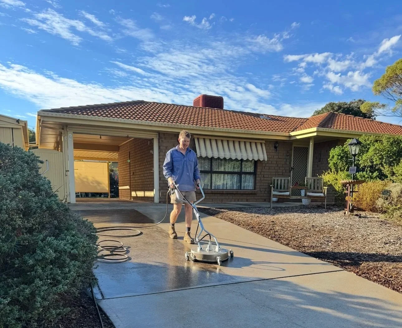 A person is pressure washing a concrete driveway in front of a house during daytime.