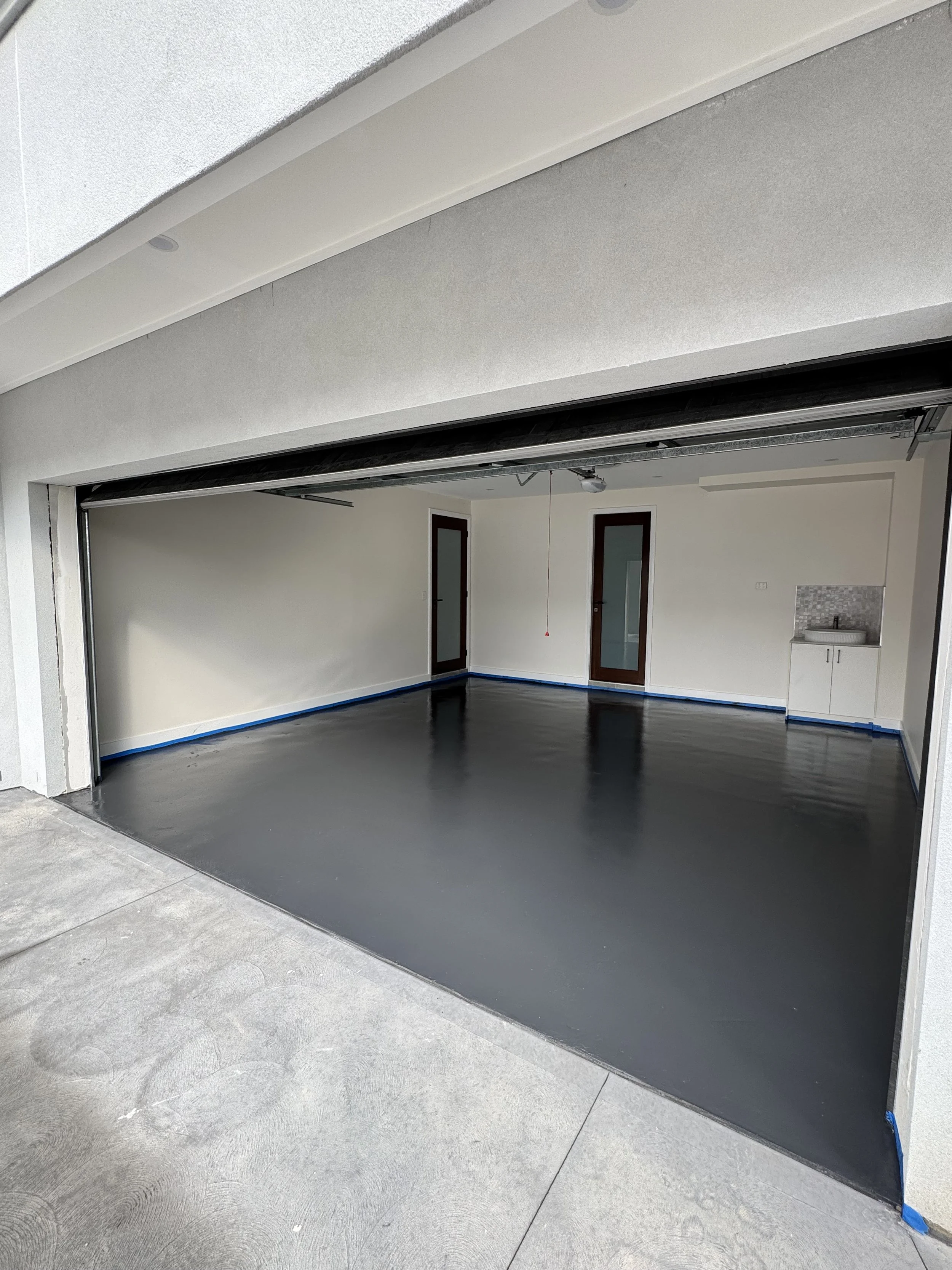 A newly constructed two-car garage with a rolling door, an interior with two doors and a small sink, and a polished concrete floor.