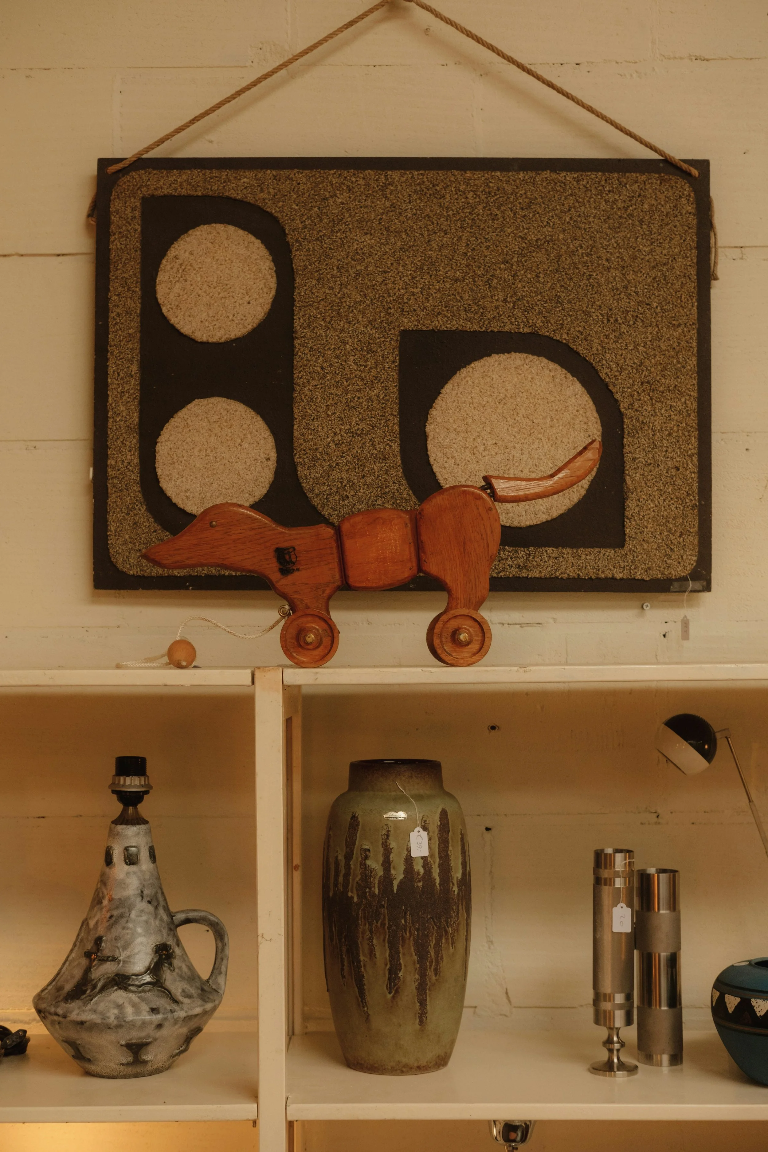 A display shelf with various decorative items including a ceramic vase, a metallic vase, a wooden dog figure, and other pottery.