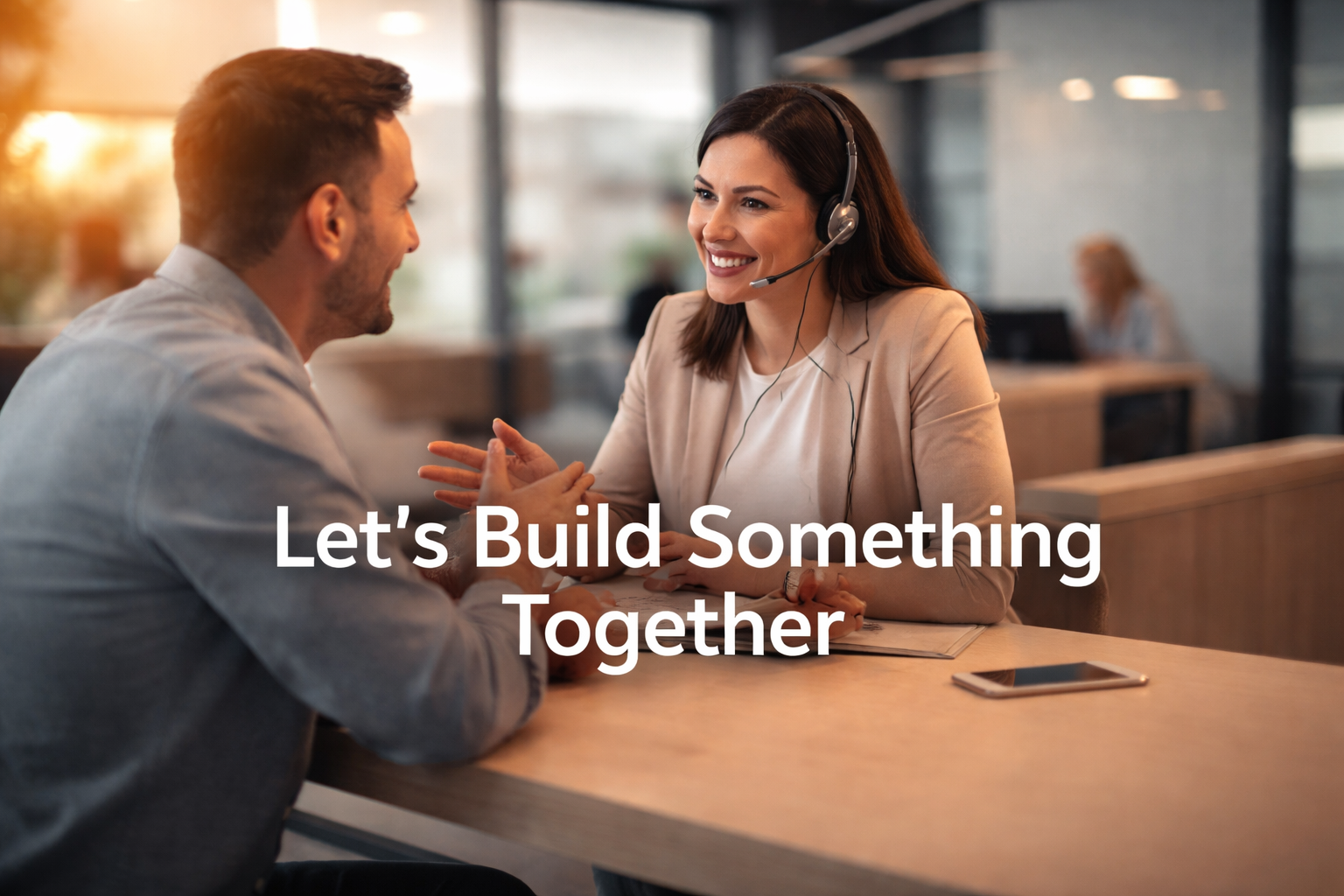 A man and woman having a conversation in an office setting, with the woman wearing a headset, and the text 'Let's Build Something Together' overlaid.