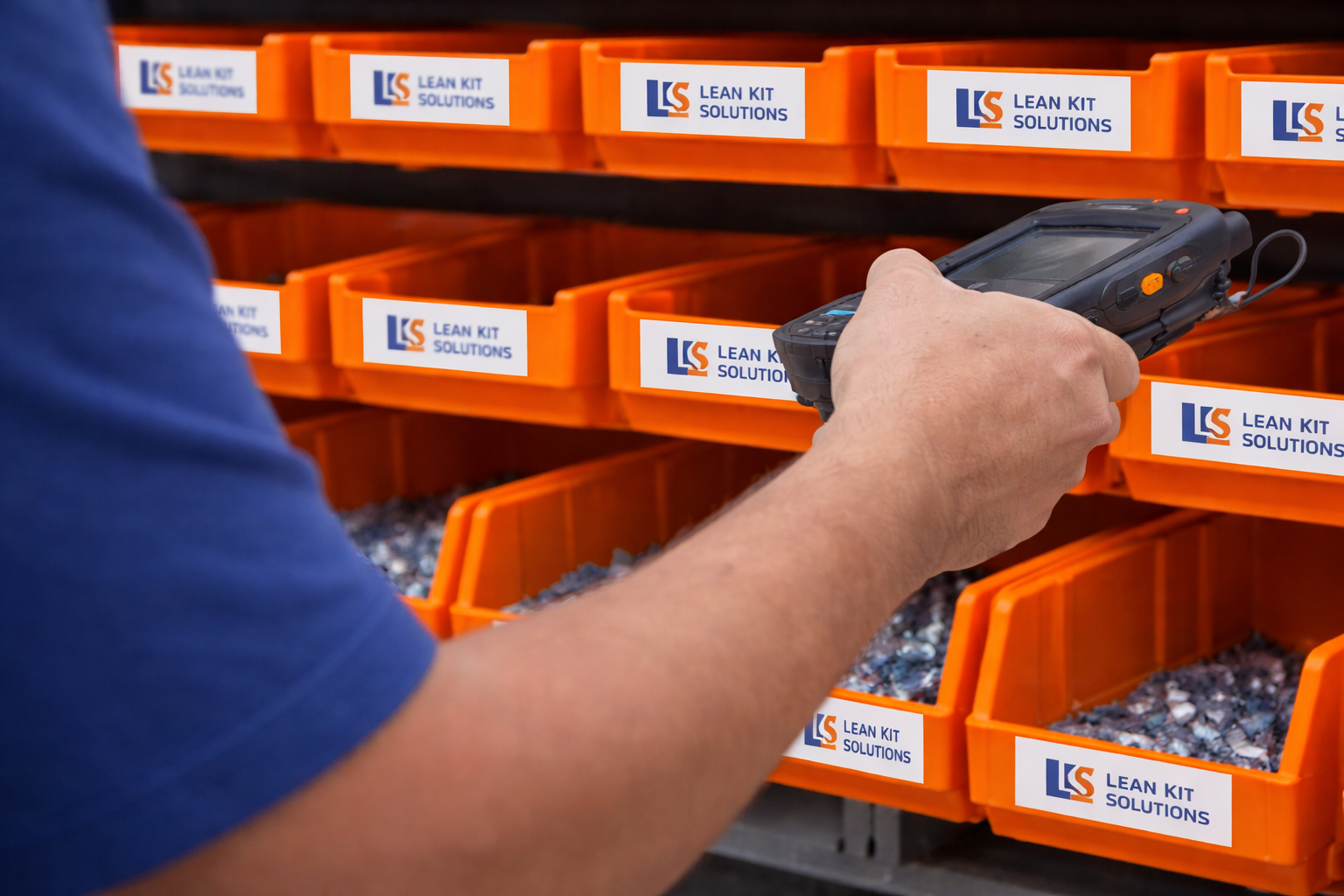 A person using a handheld device in front of orange storage bins labeled 'Lean Kit Solutions'.
