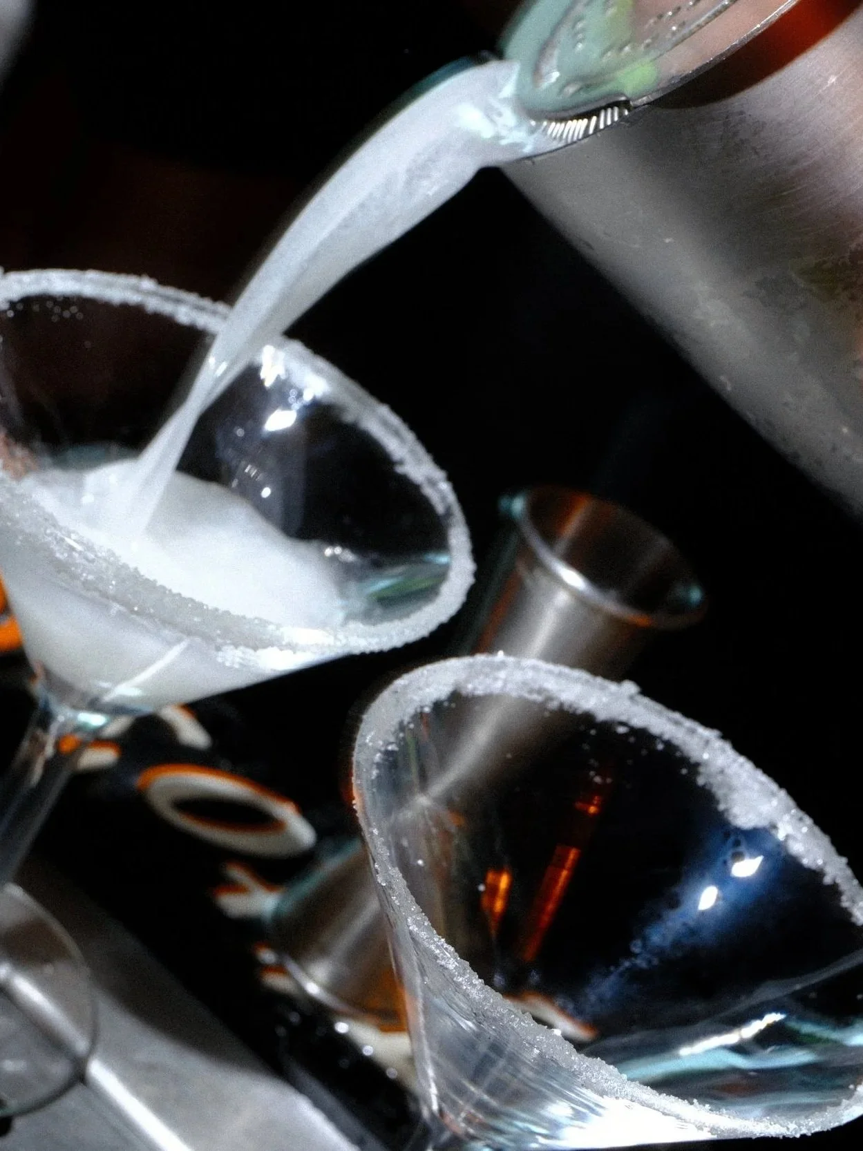 Close-up of salt-rimmed cocktail glasses filled with dark drinks and garnished with lime wedges