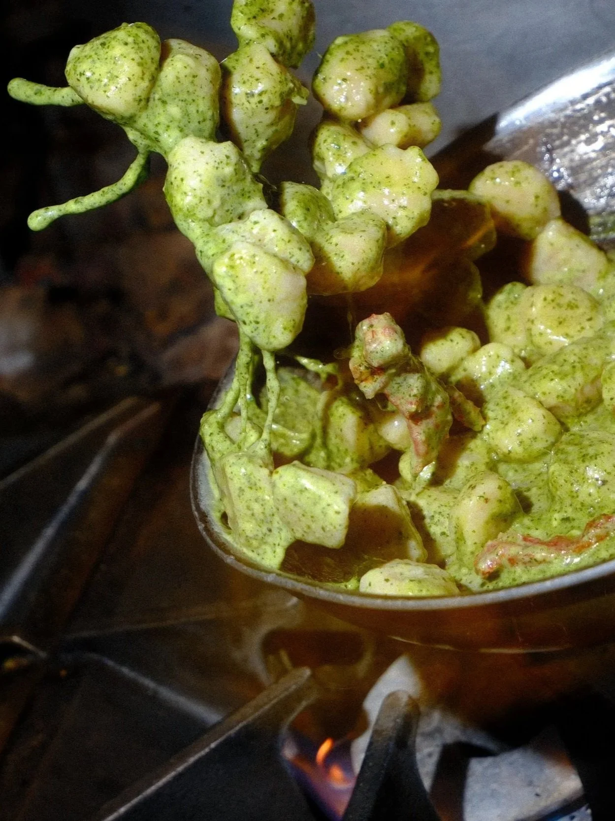Close-up of pale green, herb-coated food pieces on a metal skewer over an open flame