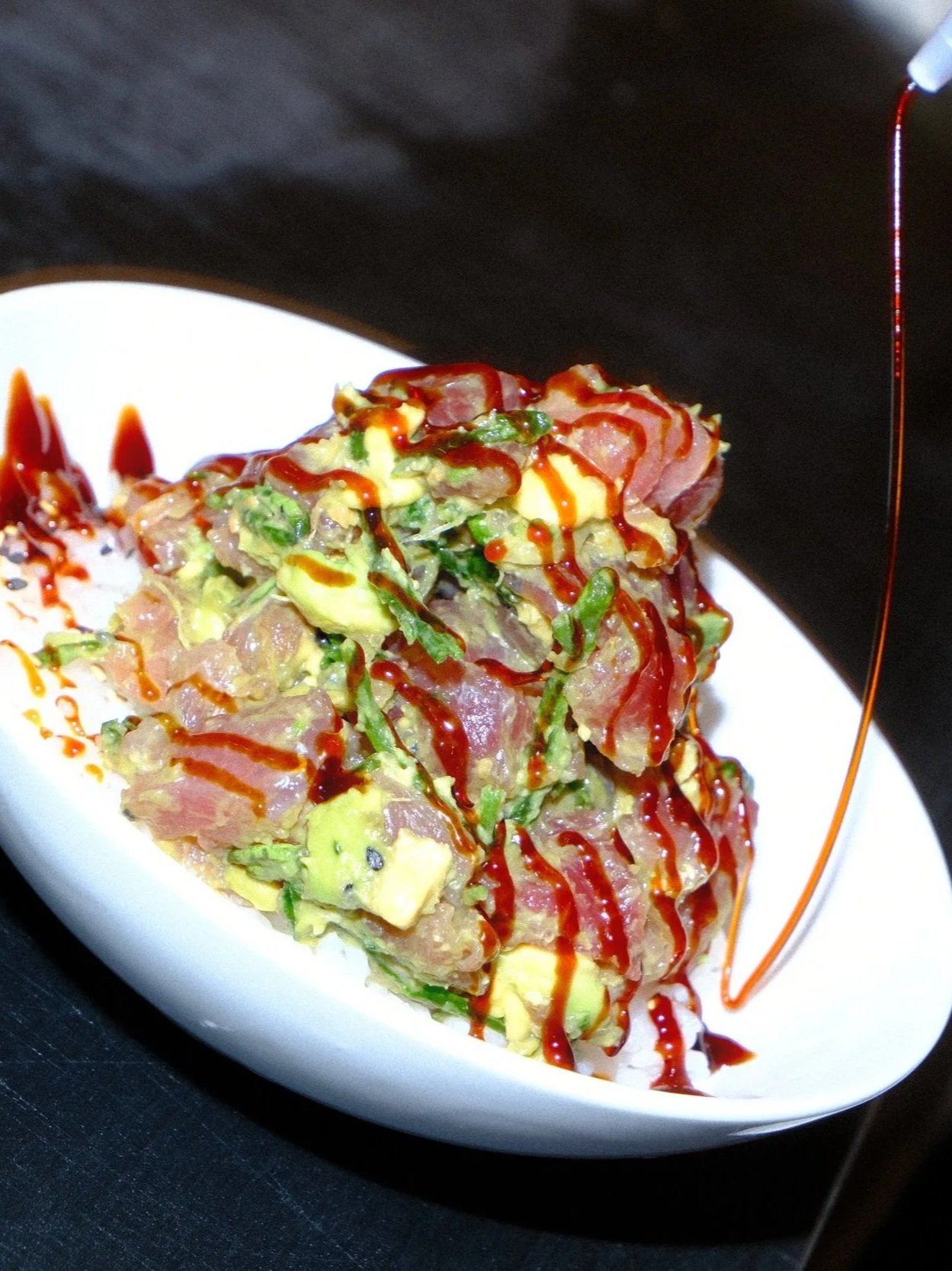 Tuna tartare with avocado, greens, and spicy red sauce on a white plate