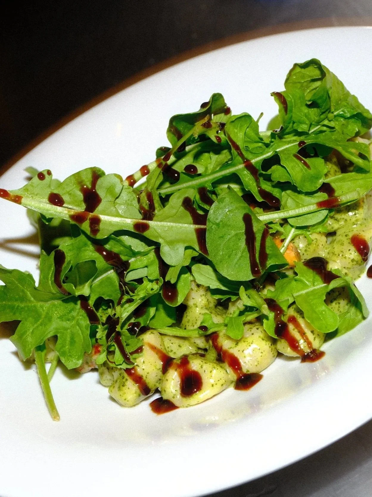 Gnocchi topped with mixed greens and drizzled with balsamic glaze on a white plate