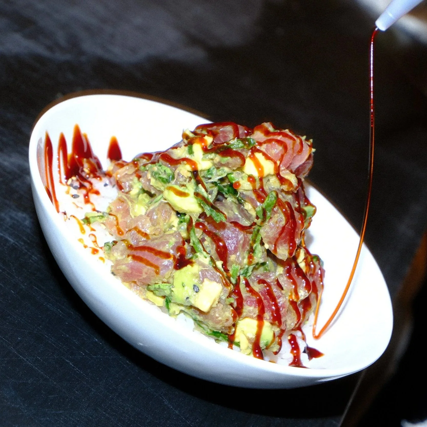 Sliced tuna poke with avocado, greens, and red sauce on a white plate