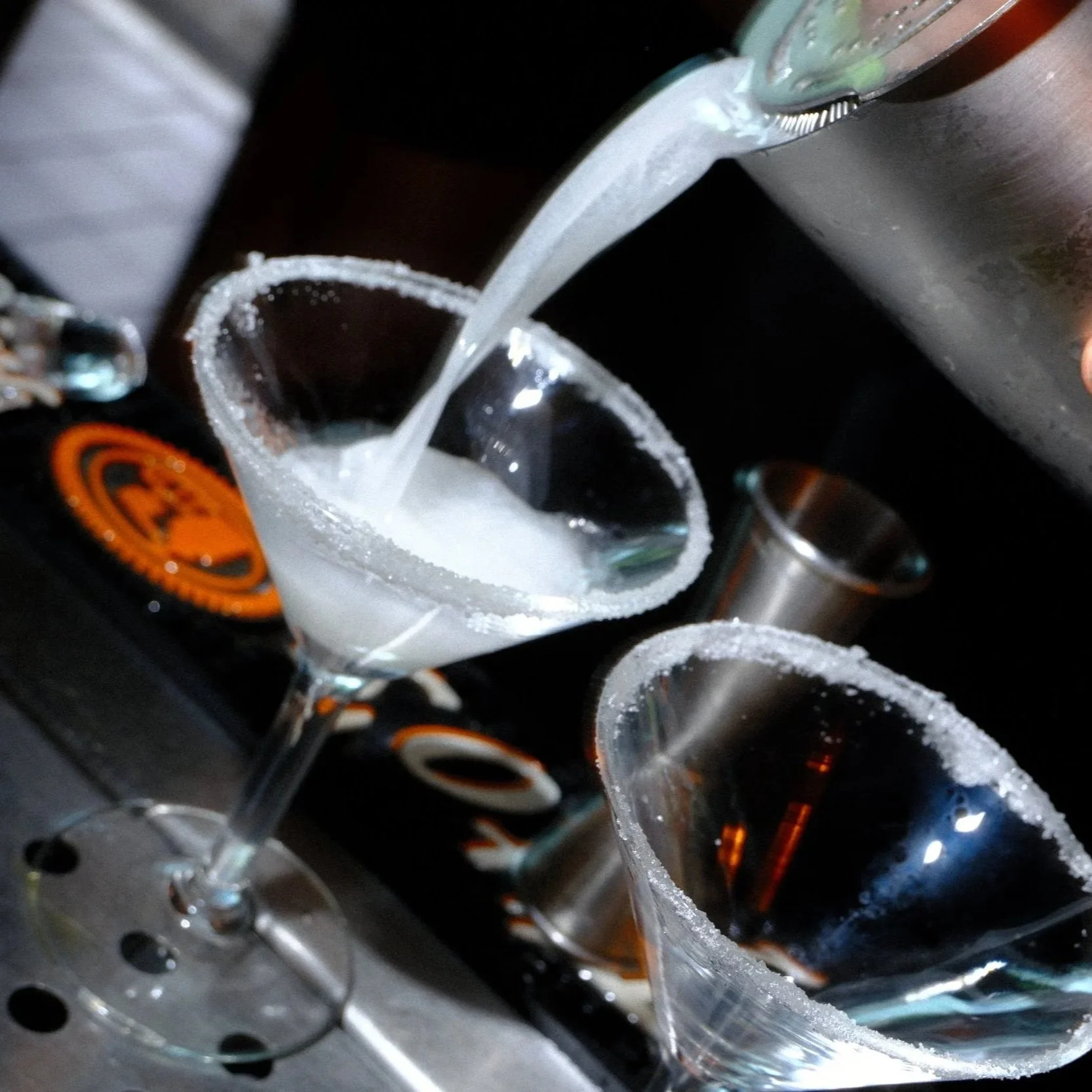 Bartender pouring a clear cocktail into a salt-rimmed martini glass