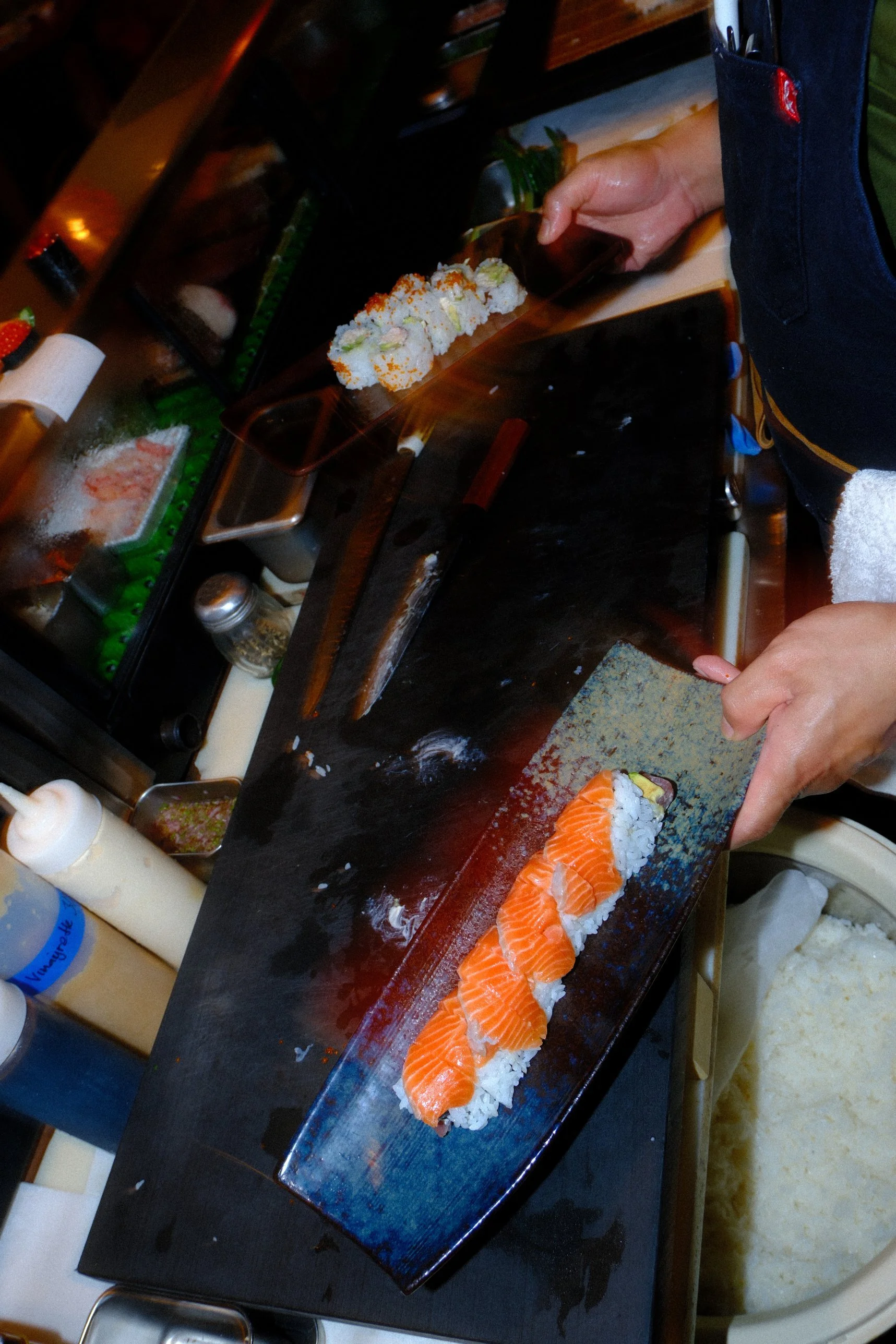 Chef preparing salmon sushi rolls on a black serving plate at a sushi restaurant