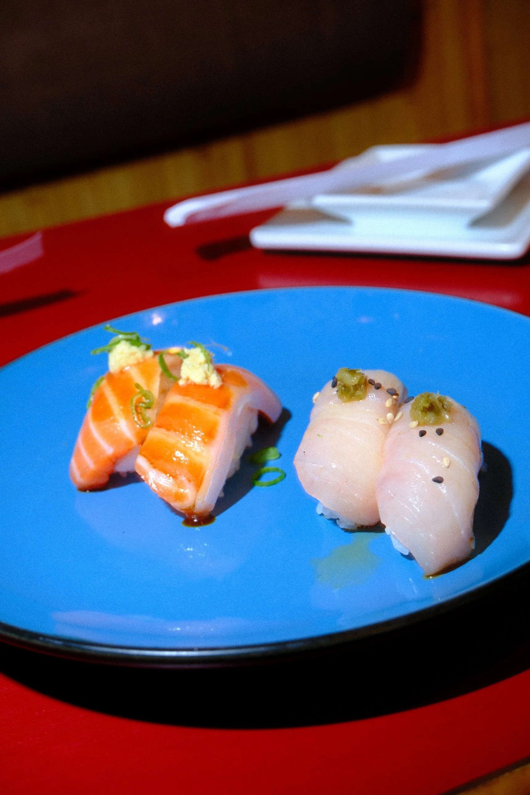 Close-up of salmon and white fish sushi topped with green garnish and sesame seeds on a blue plate