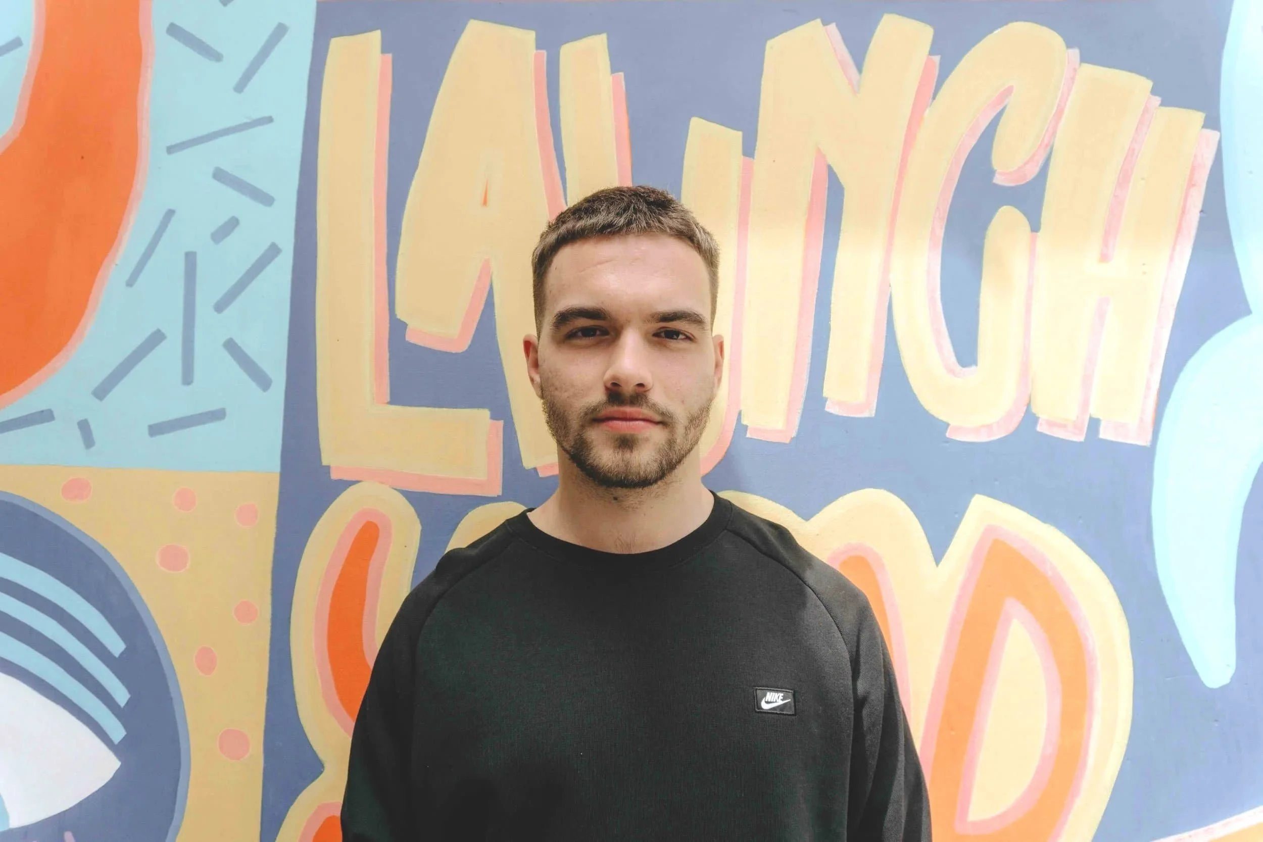 A man in a black Nike sweatshirt stands by a colorful mural, highlighting Therapy for Young Adults with bold letters and abstract shapes.