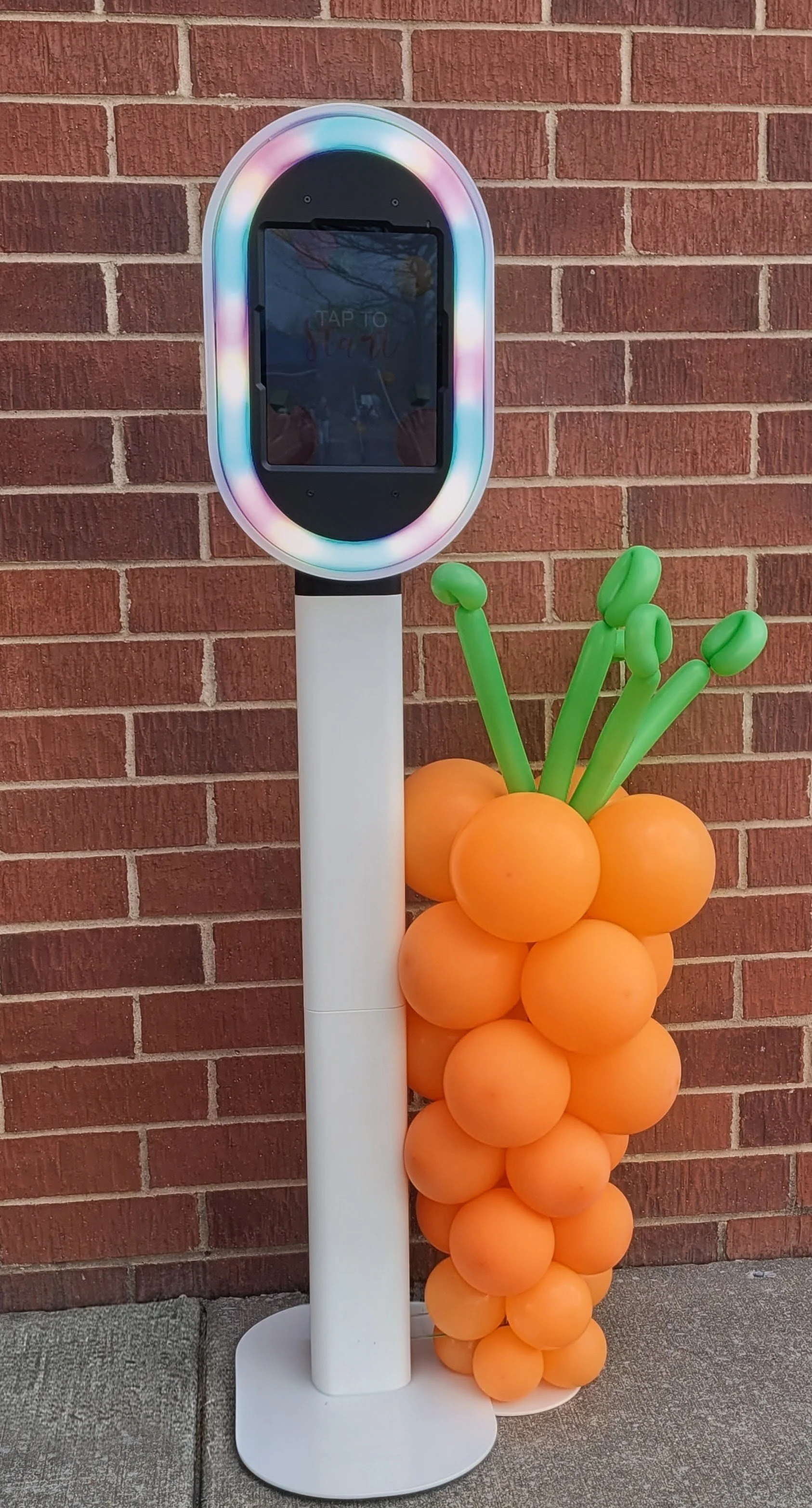A contactless payment kiosk next to a large decorative balloon sculpture shaped like a bunch of carrots.