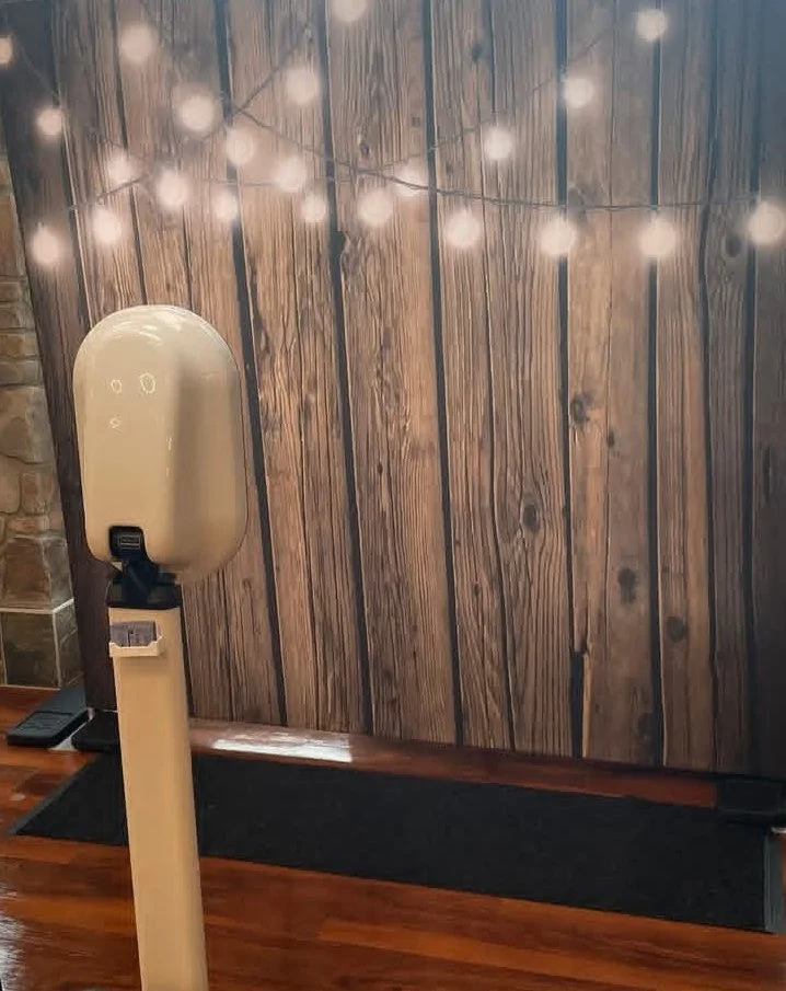 A wooden wall with string lights hanging in front, and a hand sanitizer dispenser mounted on a stand on a wooden floor.