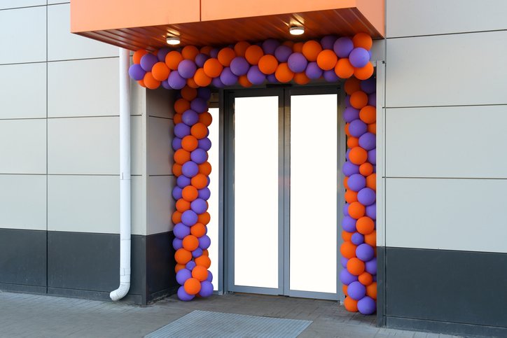 Glass door decorated with purple and orange balloons forming an arch and sides.