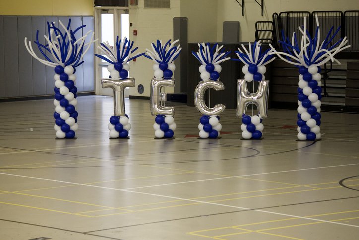 Decorative balloon pillars spelling 'TECH' on a gymnasium floor.