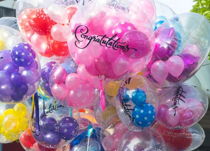 Colorful balloons with polka dots and the word 'Congratulations' written on some of them, set outdoors.
