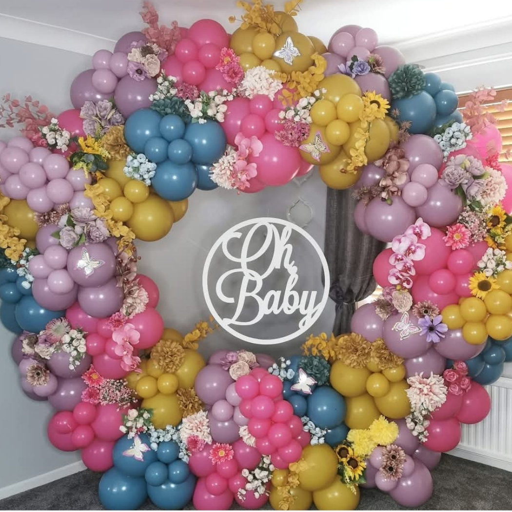 Colorful balloon display arranged in a circular shape with various flowers and a central sign that reads 'Oh Baby.'