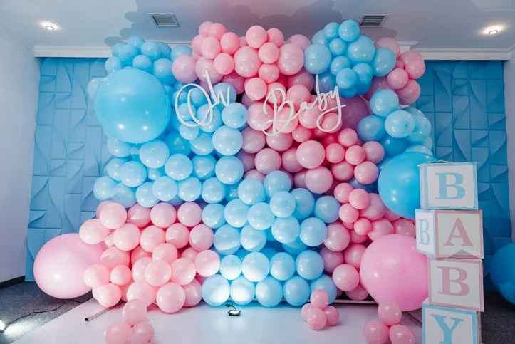 Decorative backdrop with pink and blue balloons for baby shower, featuring a white 'oh baby' sign and blocks spelling 'BABY' in pink and blue.