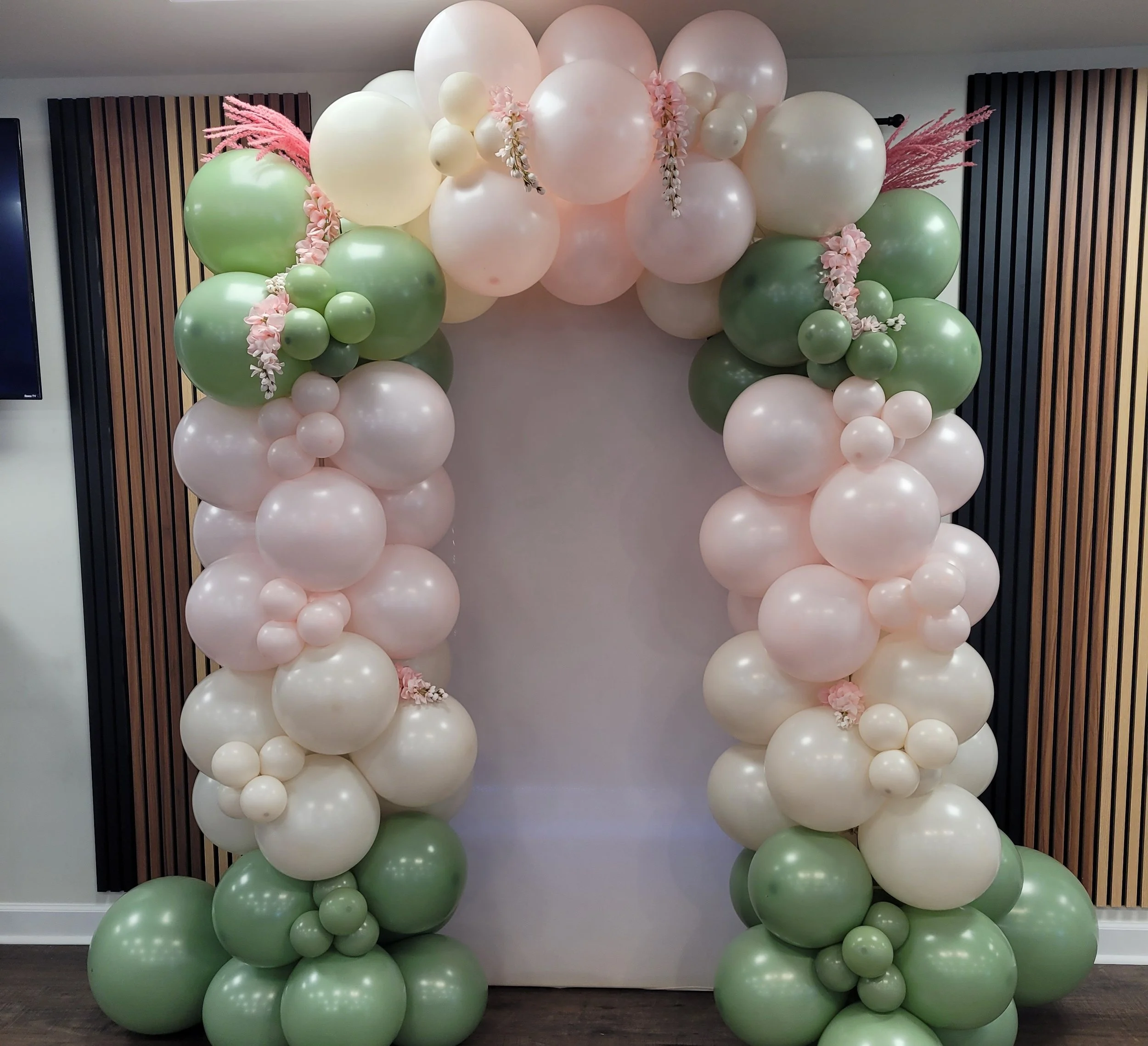 Balloon arch with pink, white, and green balloons decorated with pink flowers and pink pampas grass.