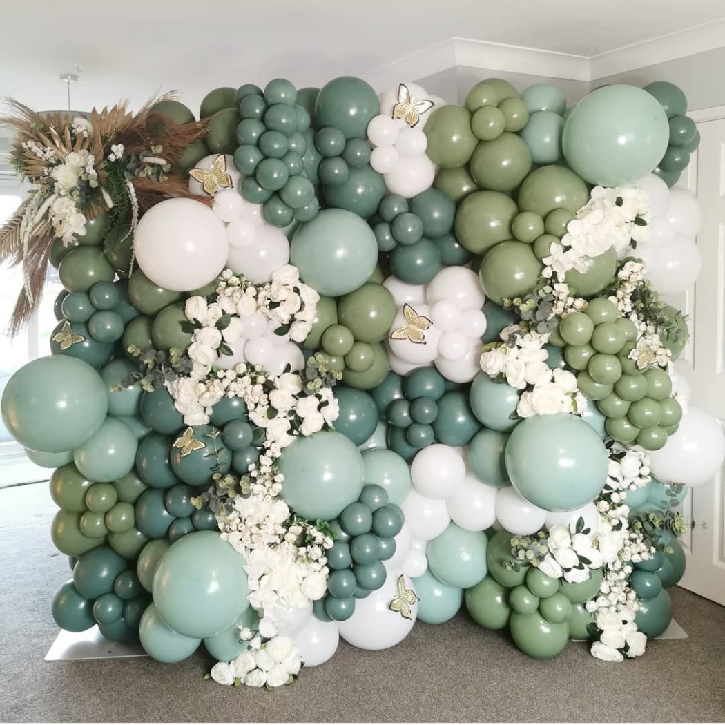 Balloon wall featuring various shades of green and white balloons, decorated with white flowers and butterfly embellishments.