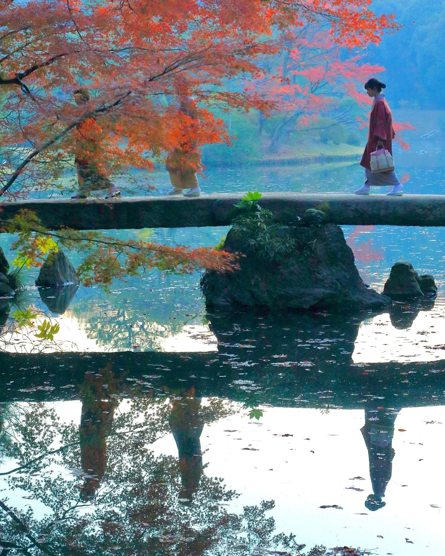 紅葉した木の下にある石橋を渡る着物を着た女性が歩いているシルエット風景。