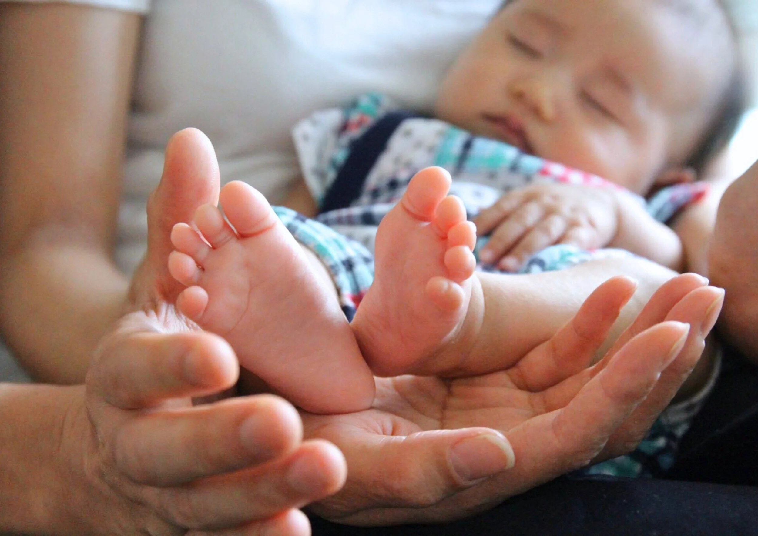 赤ちゃんの足を優しく支える両親の手と、眠っている赤ちゃんの顔