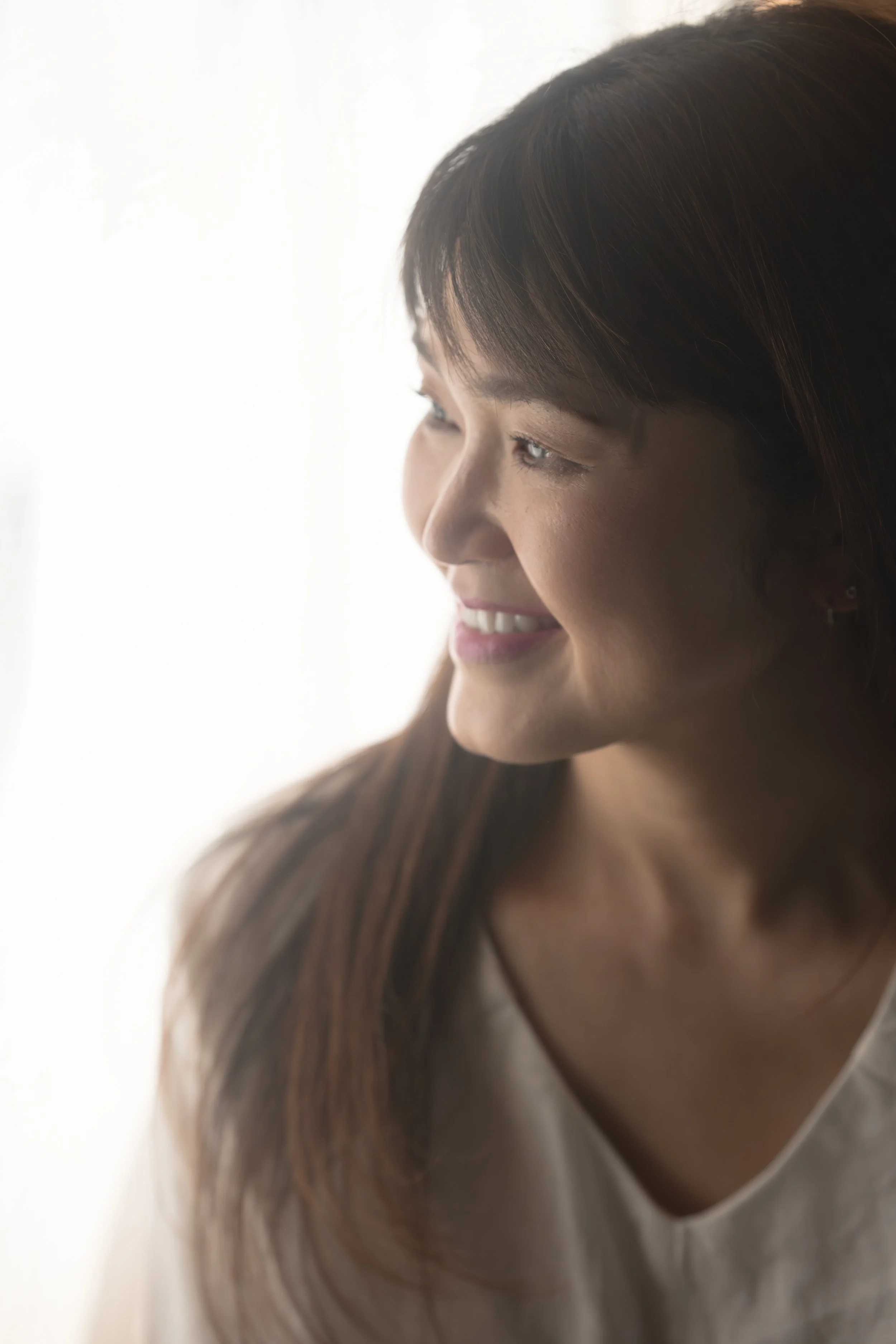 窓のそばにいる女性のプロフィール写真。微笑んでおり、自然光が彼女の顔をやわらかく照らしている。