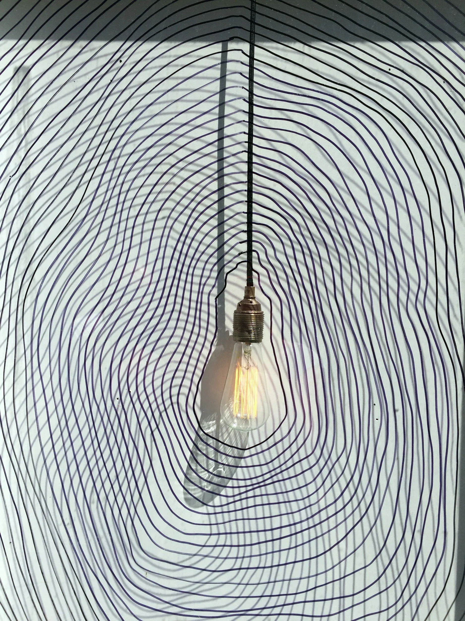 Une ampoule électrique suspendue devant un fond avec des lignes noires ondulées sur fond blanc.