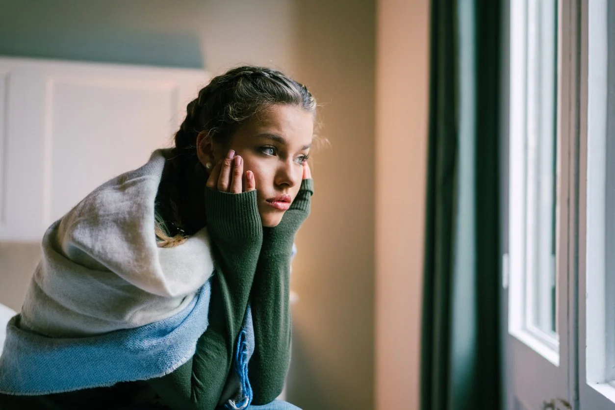 A young girl with braided hair looking out a window, resting her chin on her hands.